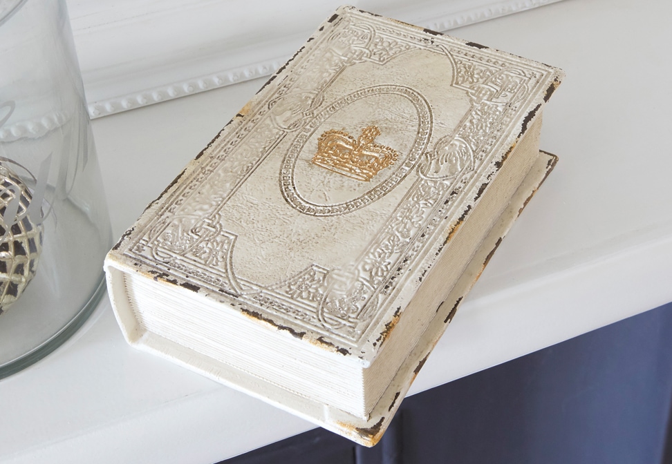 Decoratief shabby chic boek met witte verweerde kaft en gouden kroon op plank