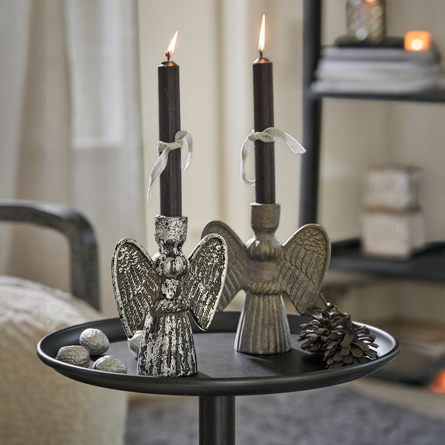 Kaarsenhouder set van 2 Auvine Twee zilverkleurige metalen engel kandelaren met zwarte kaarsen op een decoratieve tafel