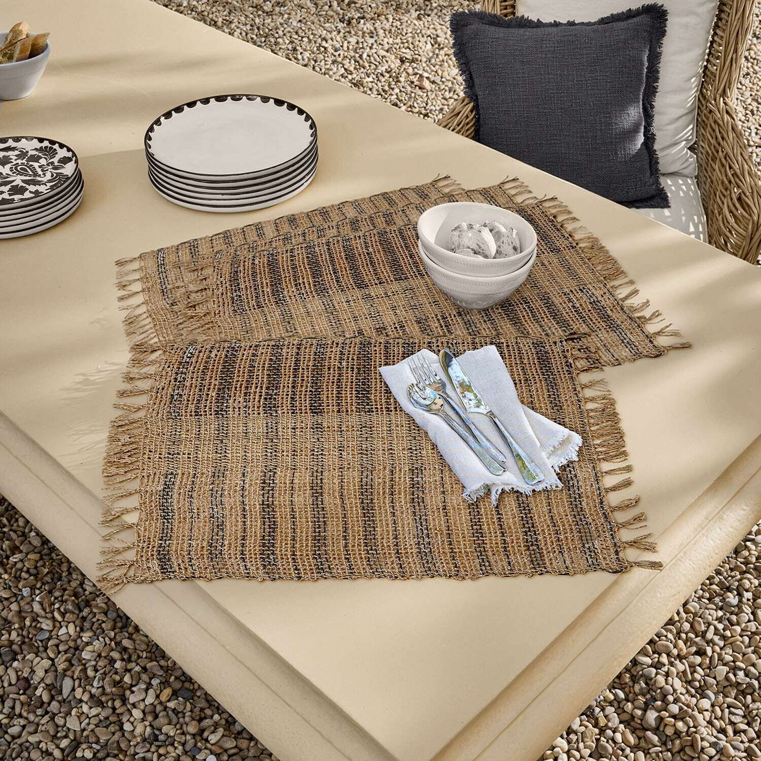 Natuurlijke jute placemats in bruin-zwarte tinten op een crèmekleurige tafel met servies en bestek