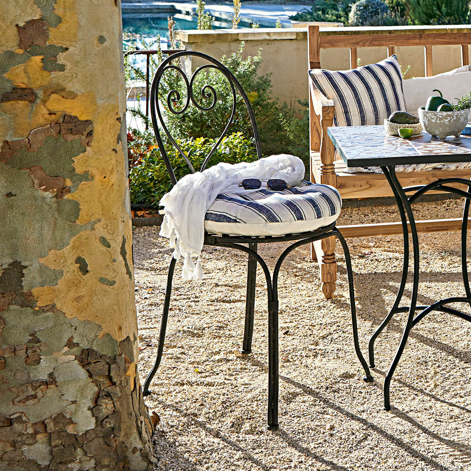 Chaise Aube Chaise de jardin en métal noir avec coussin rayé et écharpe blanche sur patio en gravier