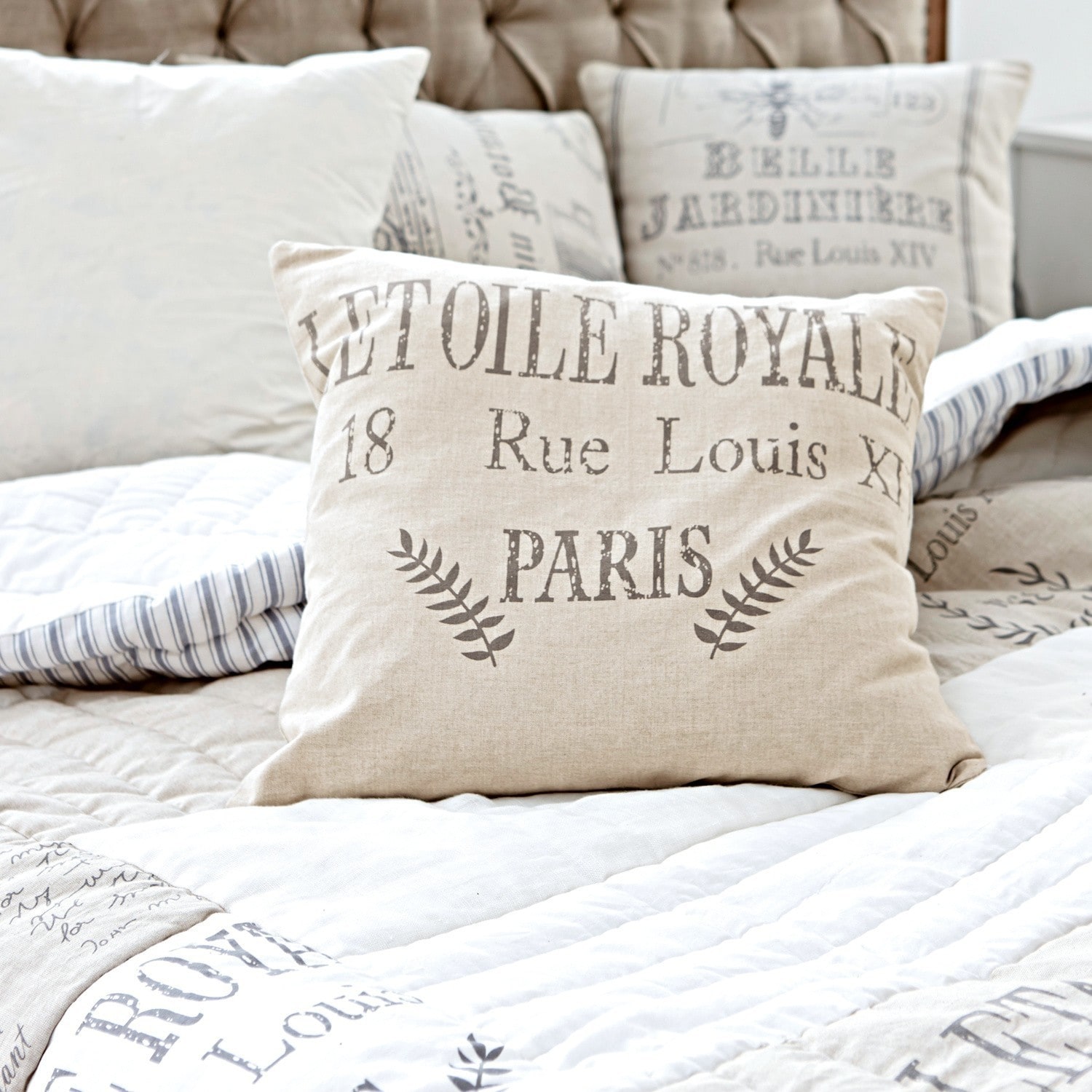 Coussin décoratif beige en lin avec impression texte vintage sur un lit confortable
