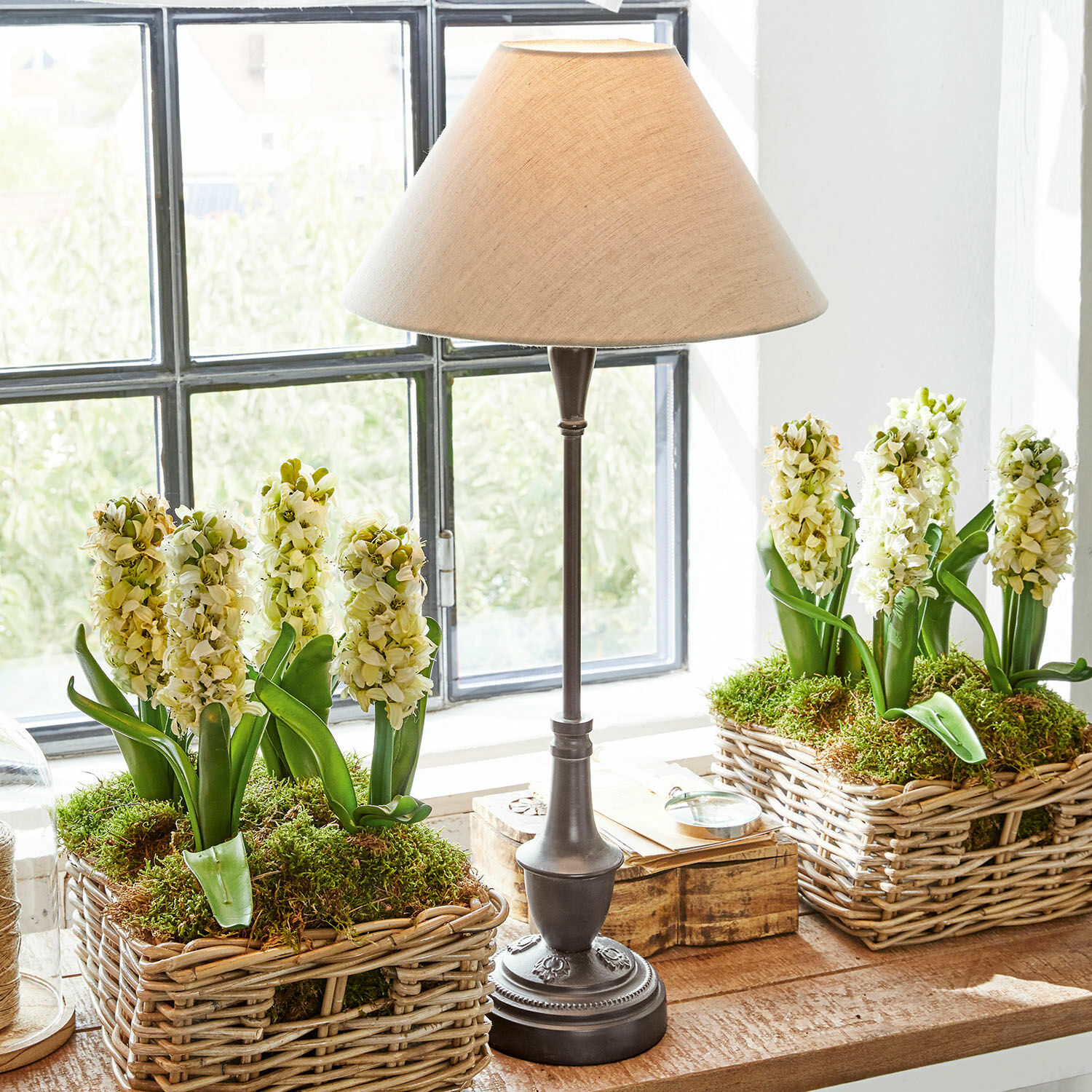 Tafellamp Barnwell Tafellamp met metalen voet en beige kap naast rieten manden met witte bloemen en mos