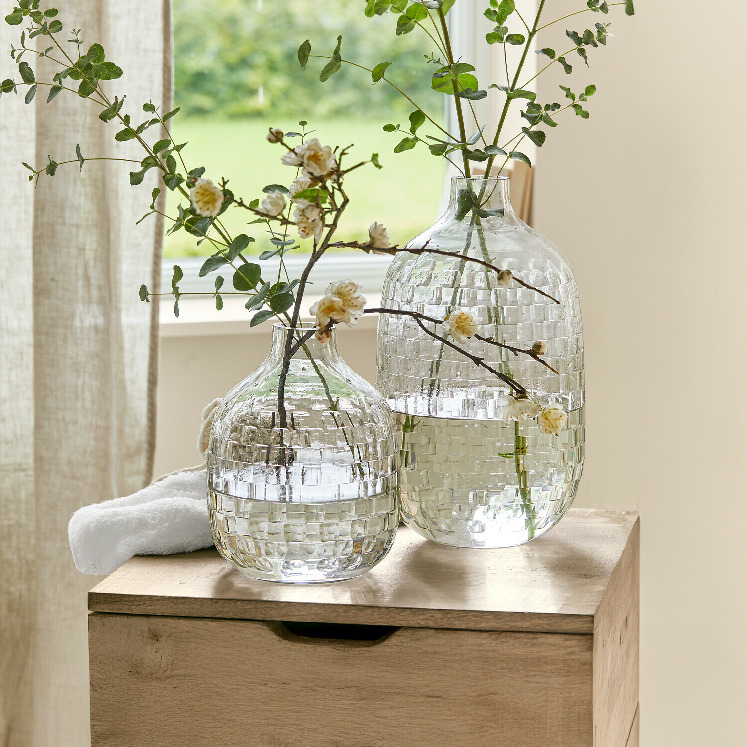 Vaas set van 2 Qervilon Twee doorzichtige glazen vazen met ruitpatroon met groene takken en bloemen op houten tafel