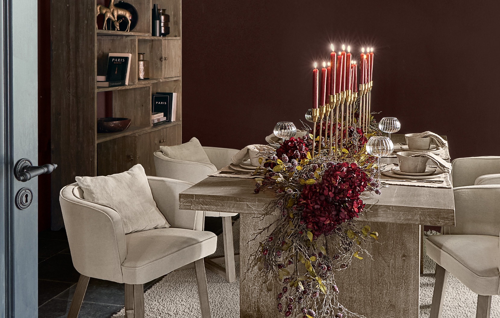 Eetkamer met houten tafel, crèmekleurige stoelen en centrale decoratie van rode kaarsen en bloemen