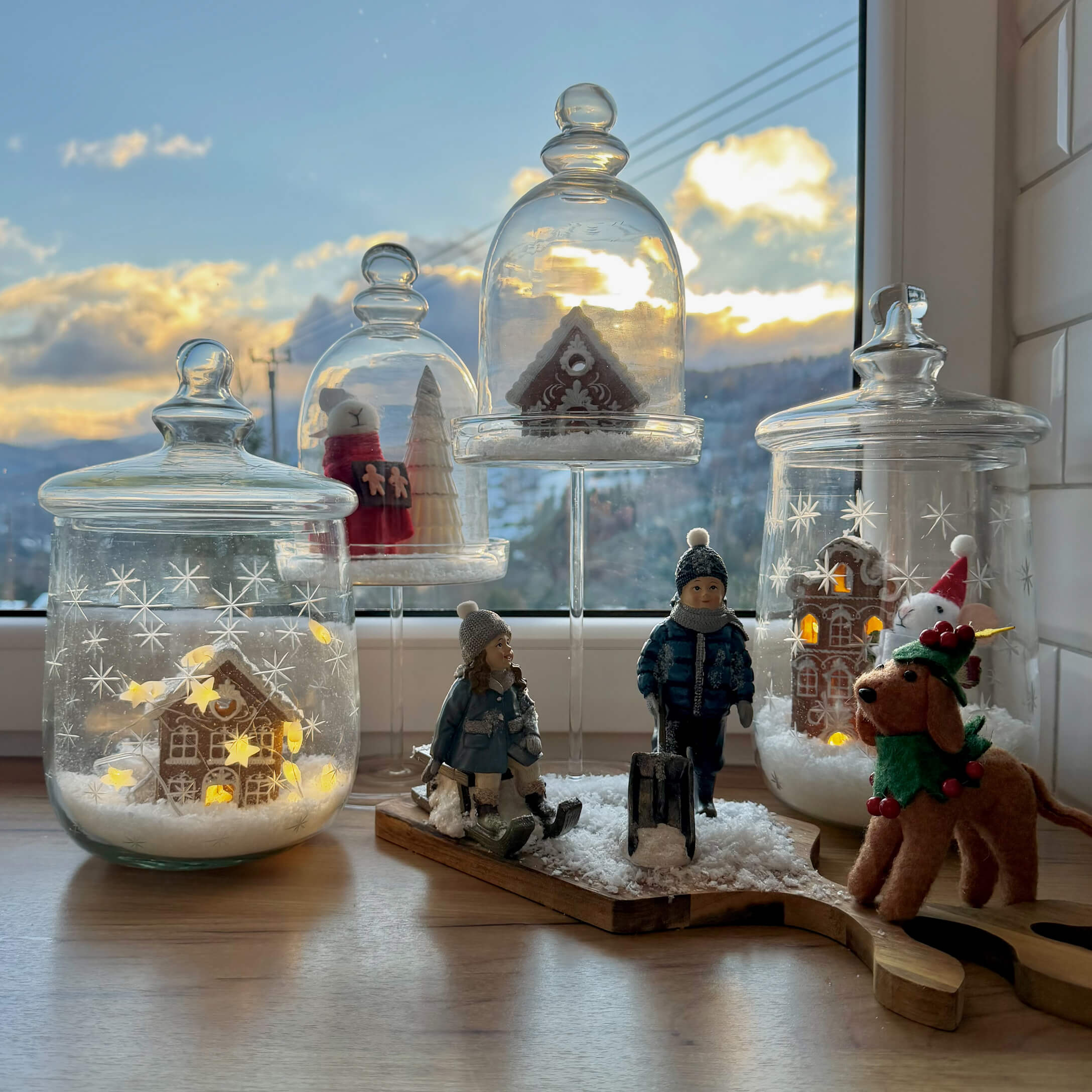 Décorations de Noël avec figurines d'enfants, chien et maisons en pain d'épice sous cloches en verre sur un rebord de fenêtre