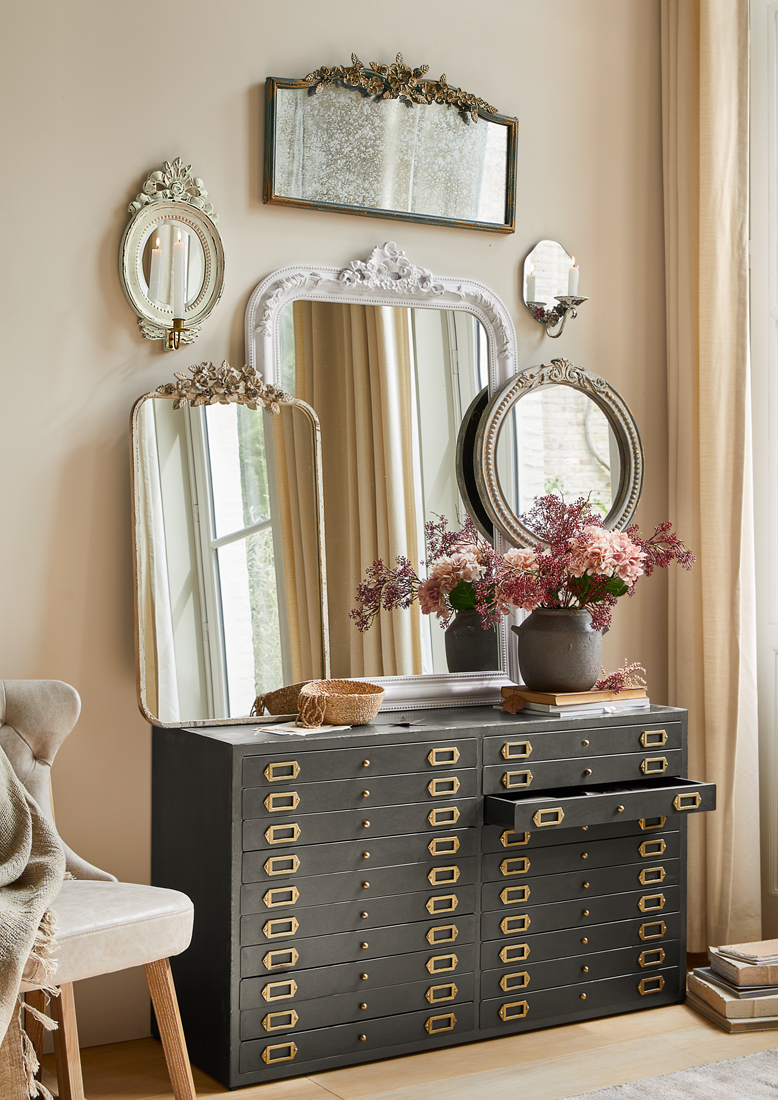 Zwarte metalen ladekast met veel lades en decoratieve vintage spiegels aan de muur