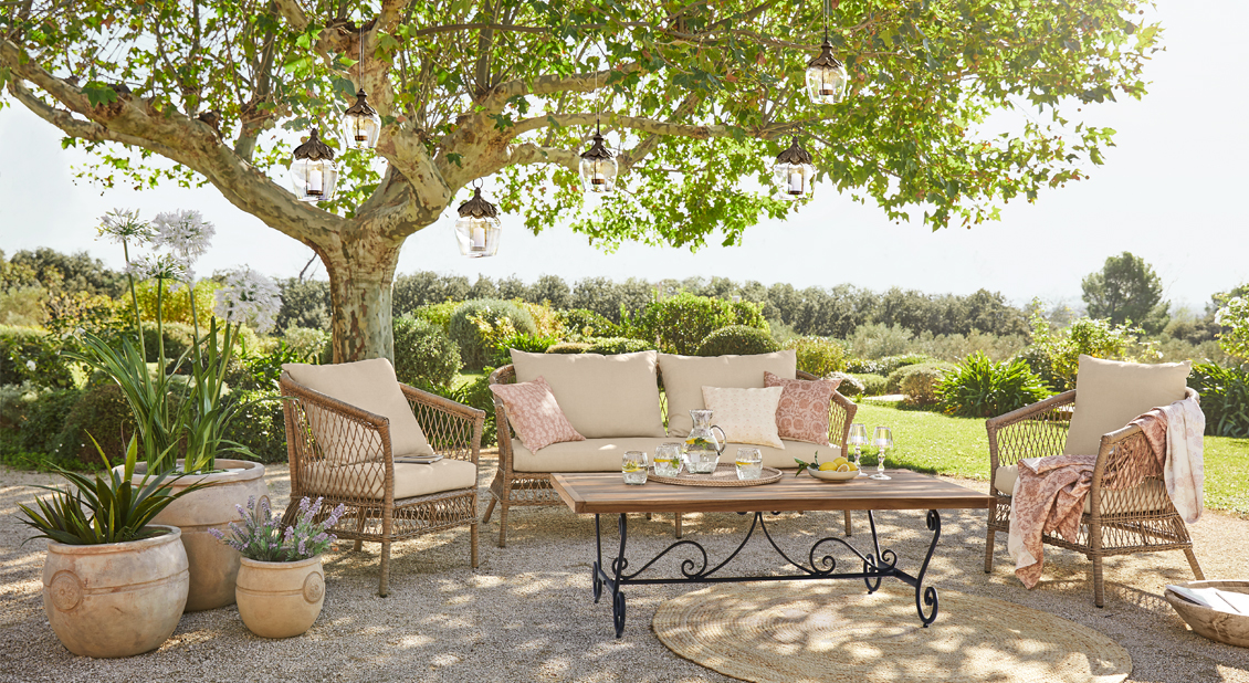 Ensemble de mobilier de jardin avec coussins beige et table en bois sous un arbre ensoleillé