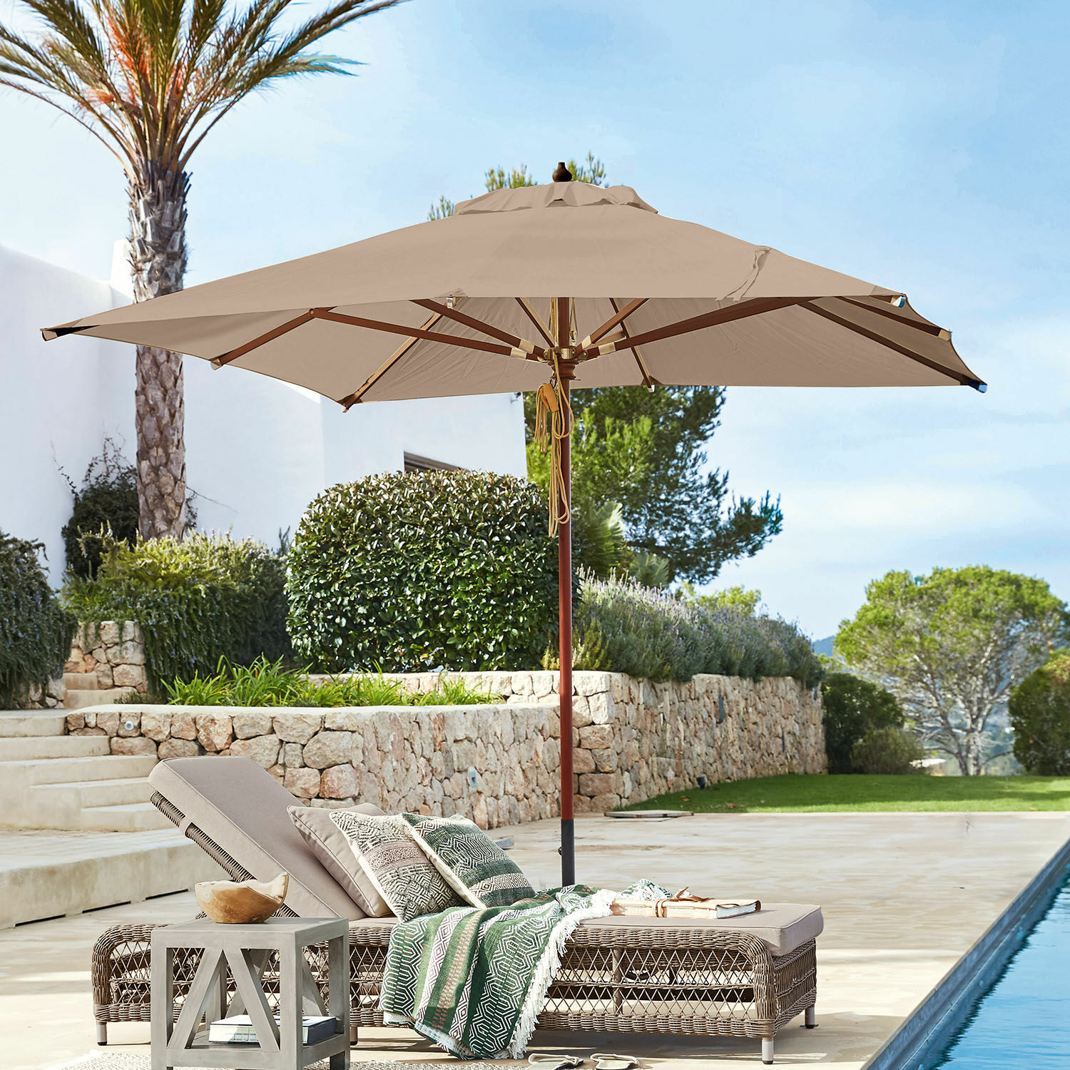 Parasol Barnet Beige tuinparasol met houten frame boven rotan ligstoel bij het zwembad