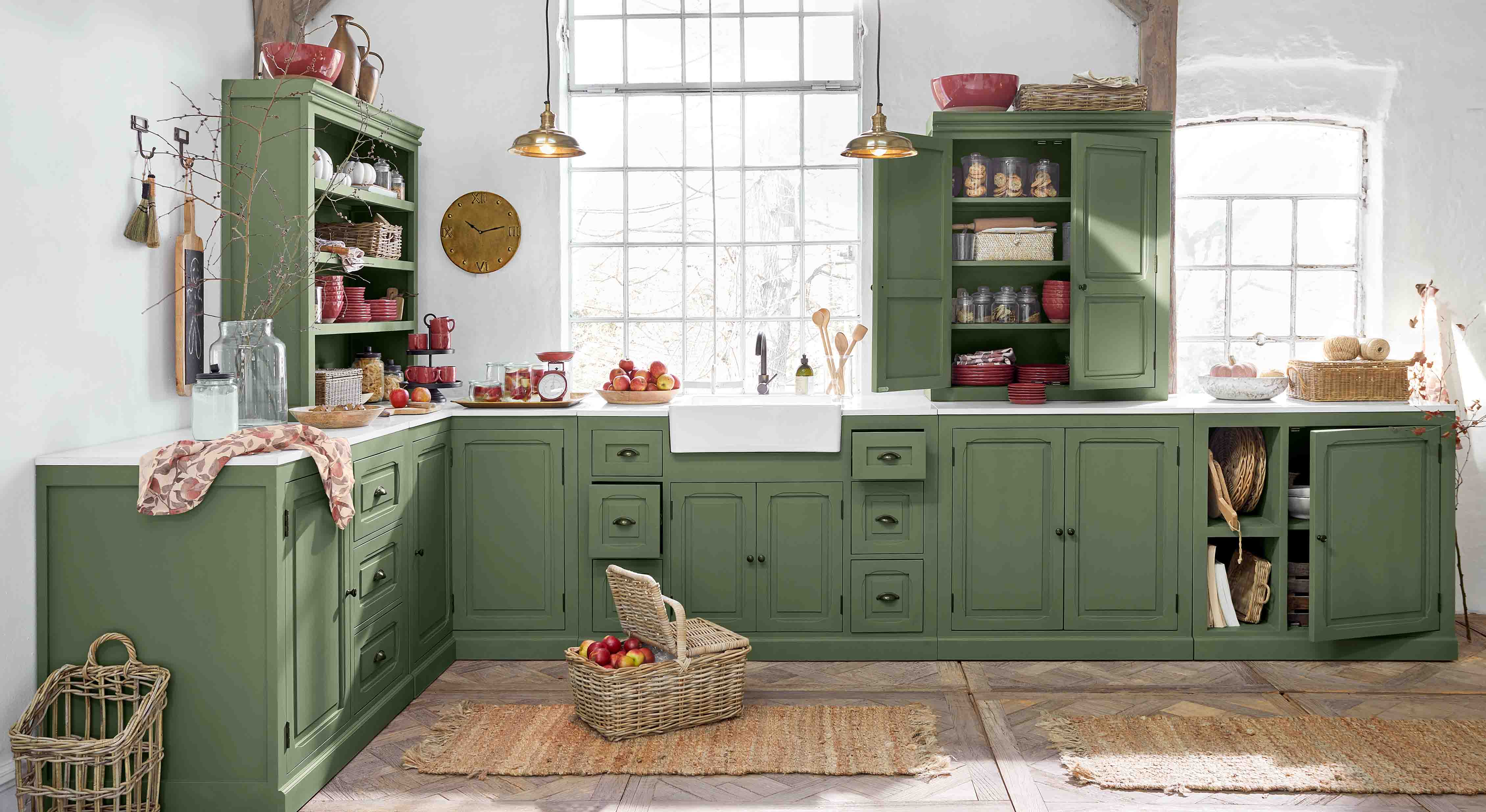 Keuken met groene houten kasten en wit aanrecht, rustieke accessoires en mand met appels