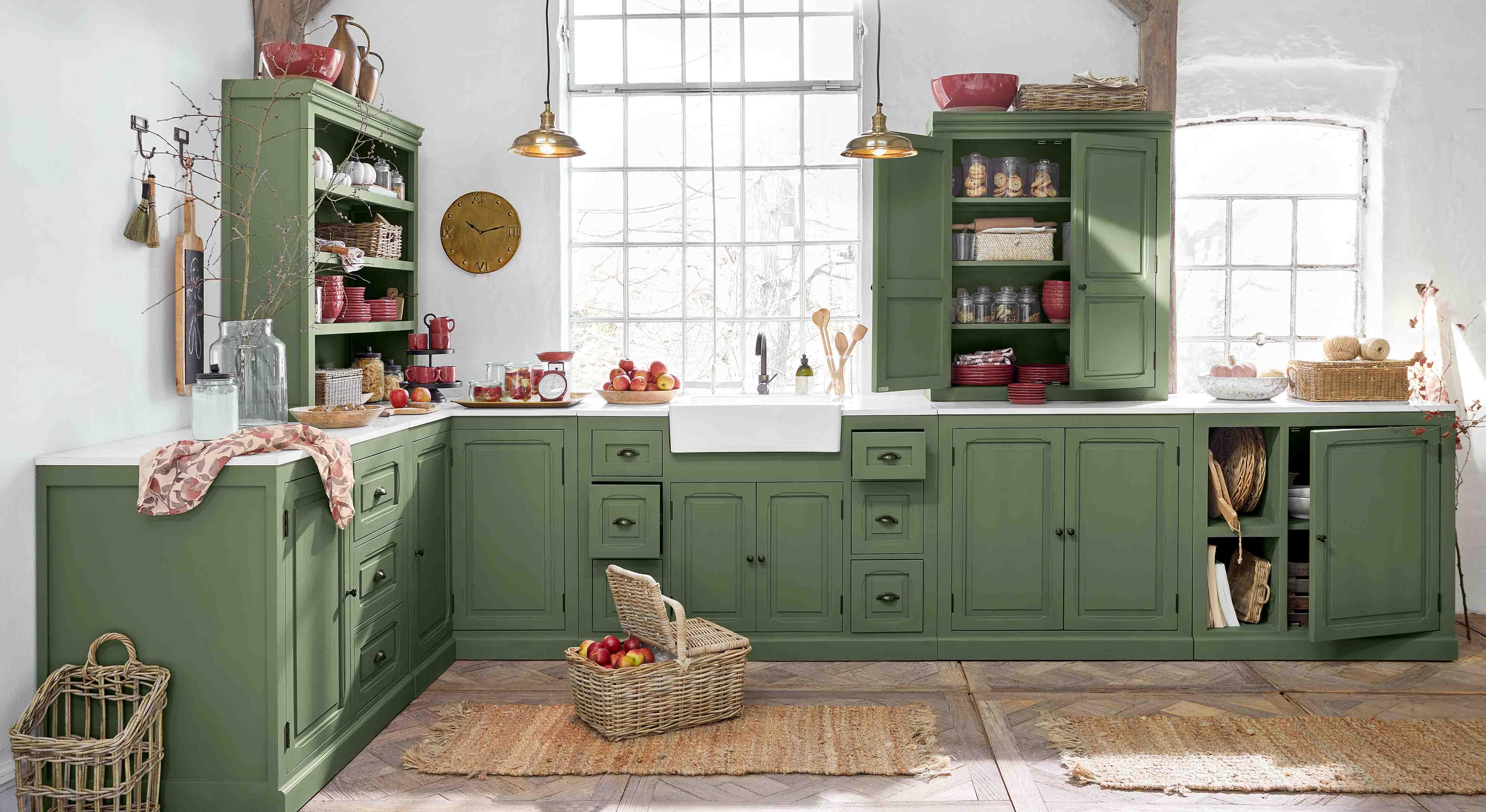 Keuken met groene houten kasten en wit aanrecht, rustieke accessoires en mand met appels