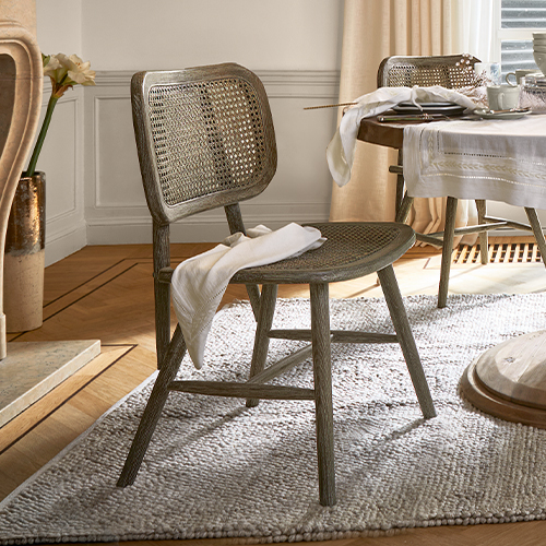Chaise en bois et rotin couleur naturelle sur tapis dans un salon lumineux avec table dressée