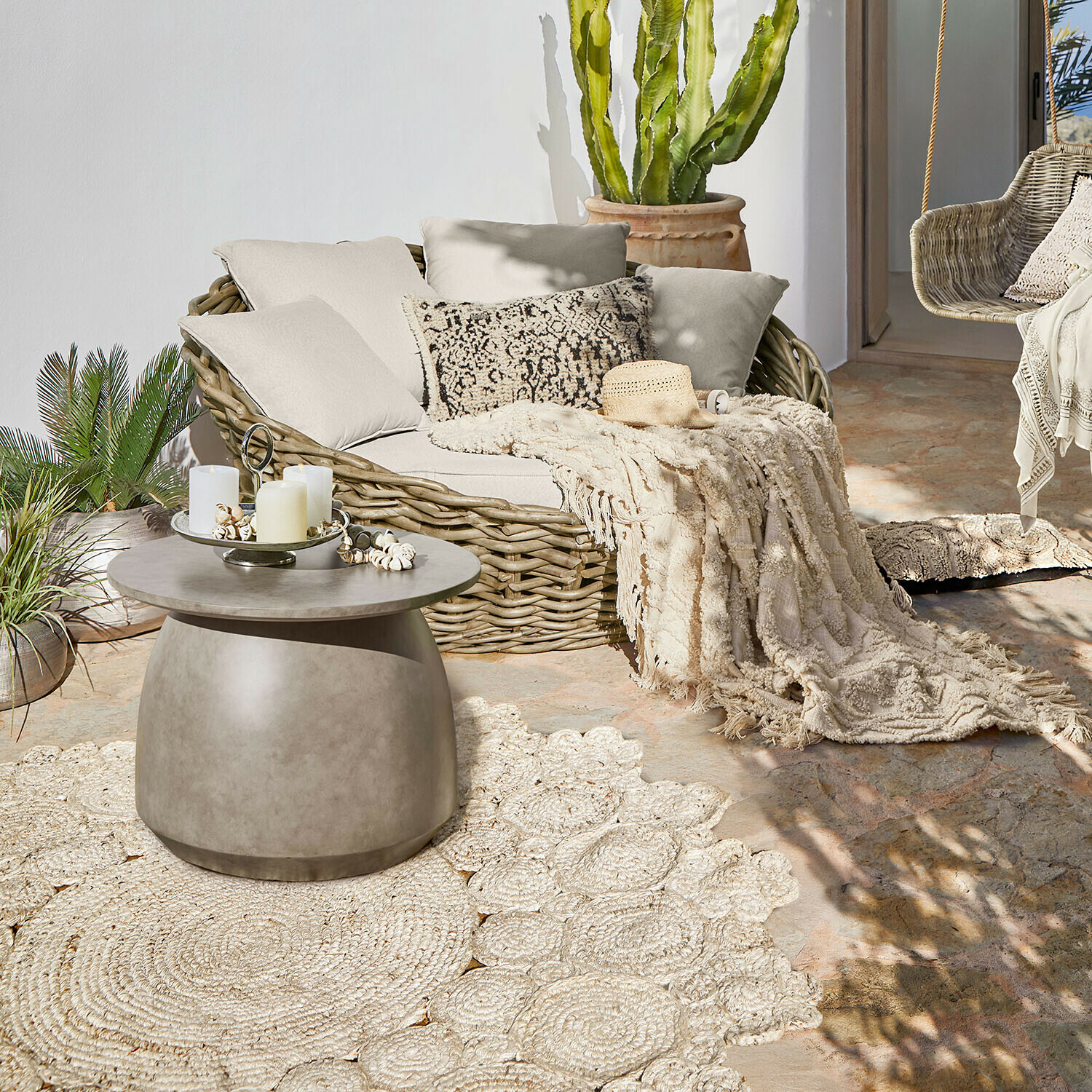 Tapis d’intérieur et d’extérieur Norlinn Canapé ovale en rotin avec coussins crème et plaid sur terrasse avec table basse en béton