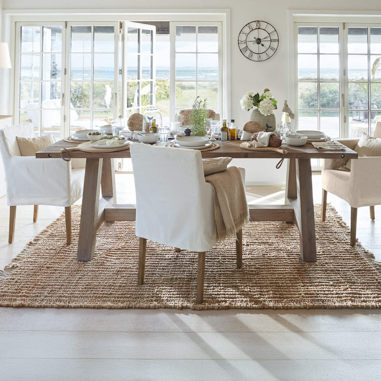 Table Berrien Salle à manger avec table en bois et chaises blanches sur tapis naturel avec vue sur jardin et mer