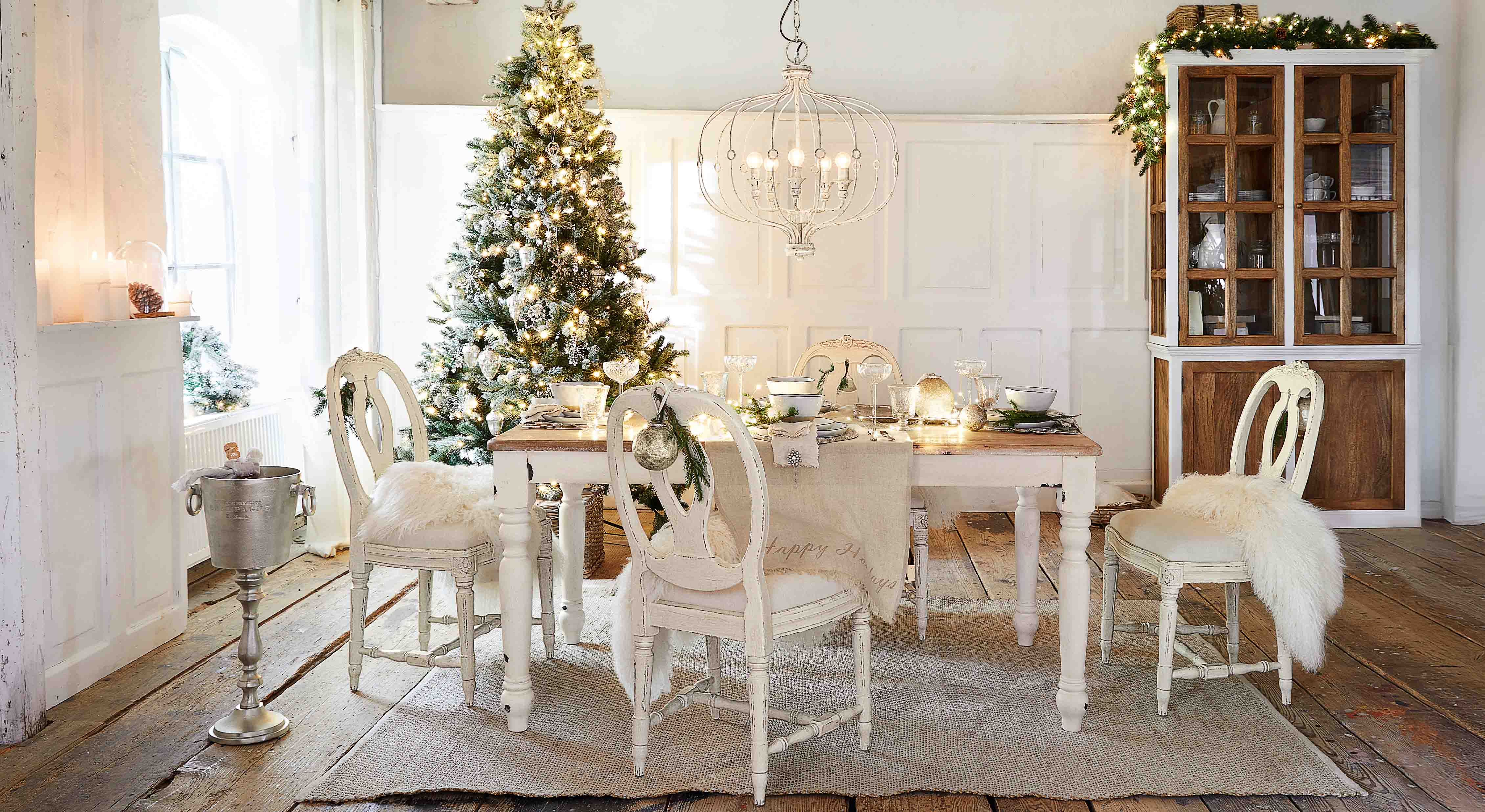 Eetkamer met witte houten tafel en stoelen, feestelijk versierd met kerstboom en lichtjes