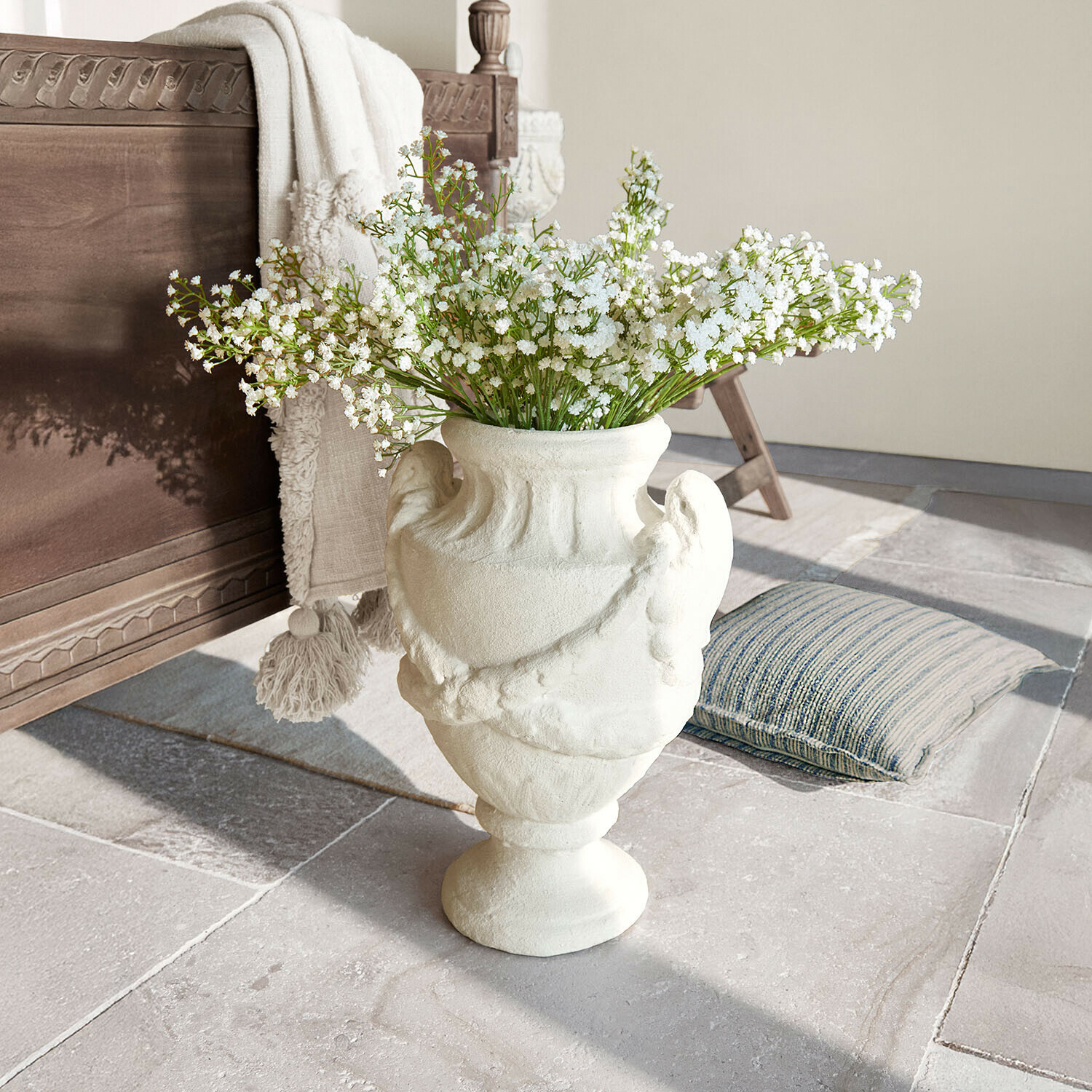 Vase en céramique blanche avec motif décoratif et fleurs blanches sur sol en pierre