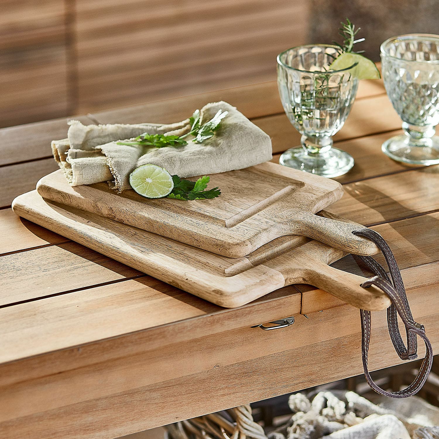 Snijplank set van 2 Lestino Houten snijplanken met handvatten en leren riemen op een tafel van natuurlijk hout