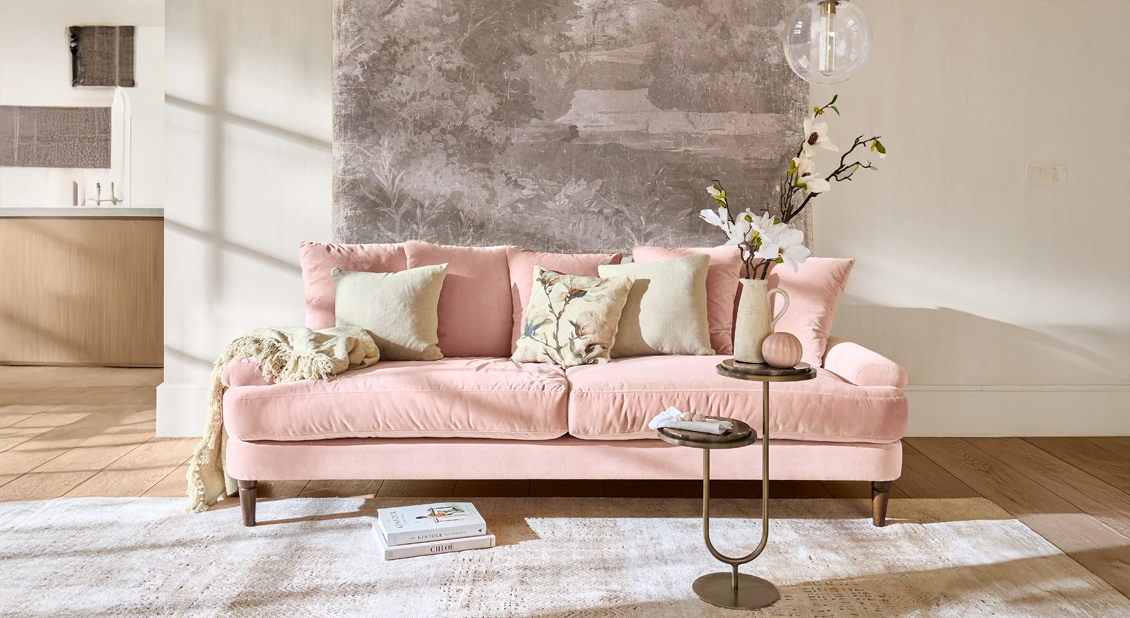 Canapé rose en velours avec coussins et table d'appoint dans un salon lumineux et moderne