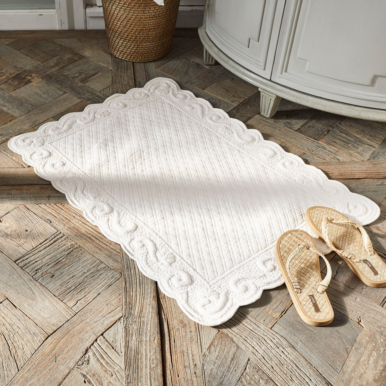 Tapis de bain Svikola Tapis décoratif blanc en coton matelassé posé sur un sol en bois avec des sandales tressées