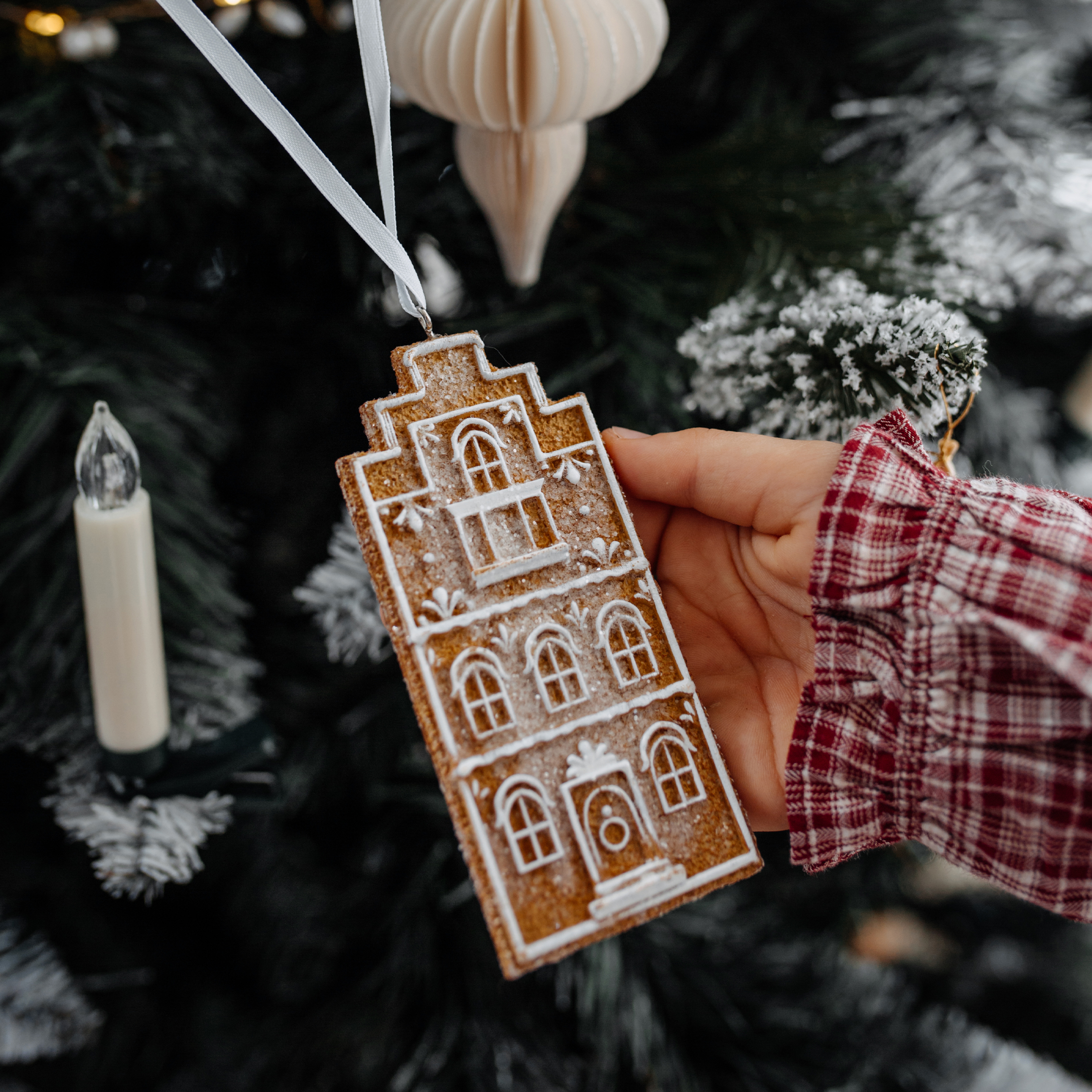Décoration de sapin en forme de maison en pain d'épice avec motifs blancs, suspendue à un ruban blanc