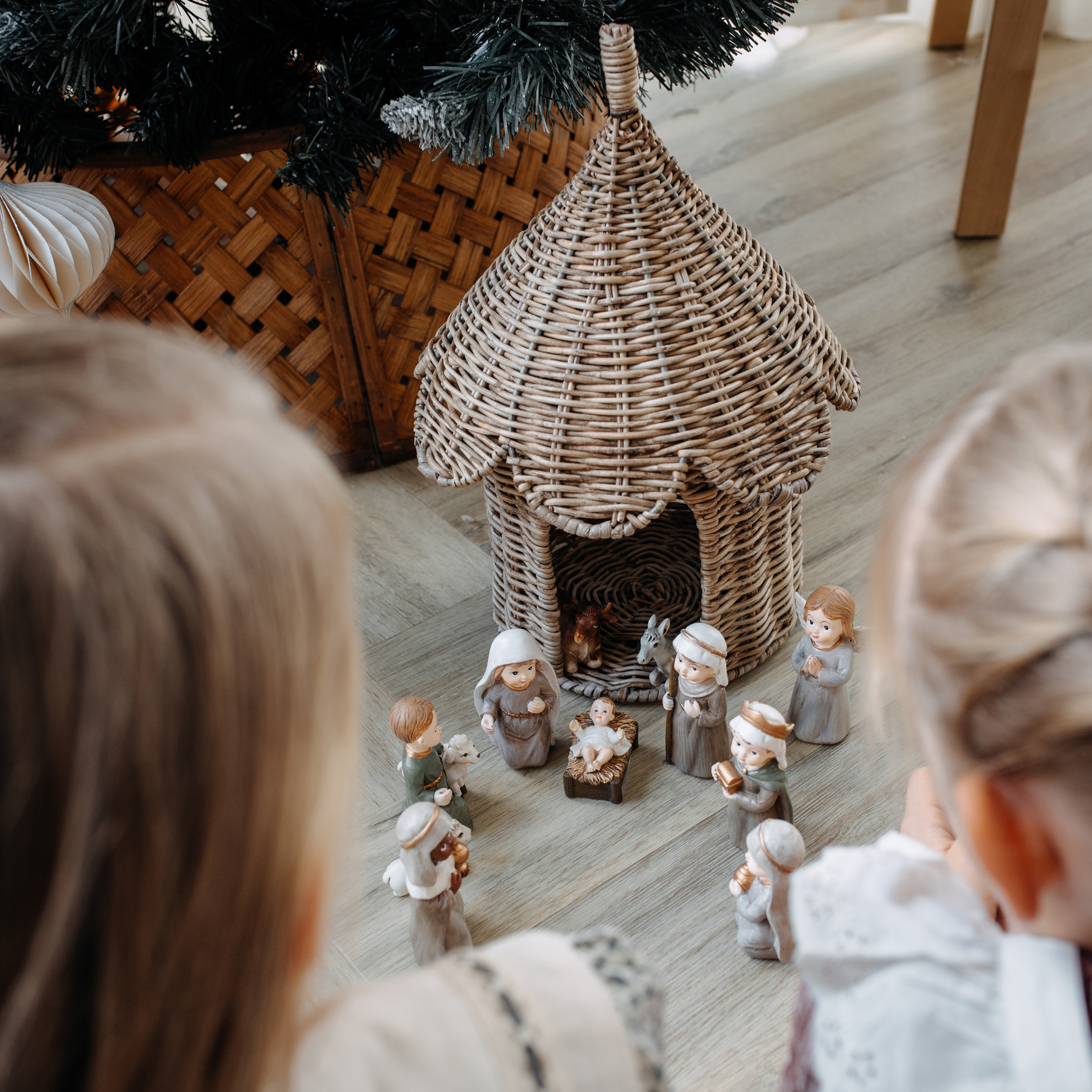 Enfants regardant une crèche de Noël avec figurines en céramique et maison en osier sur le sol