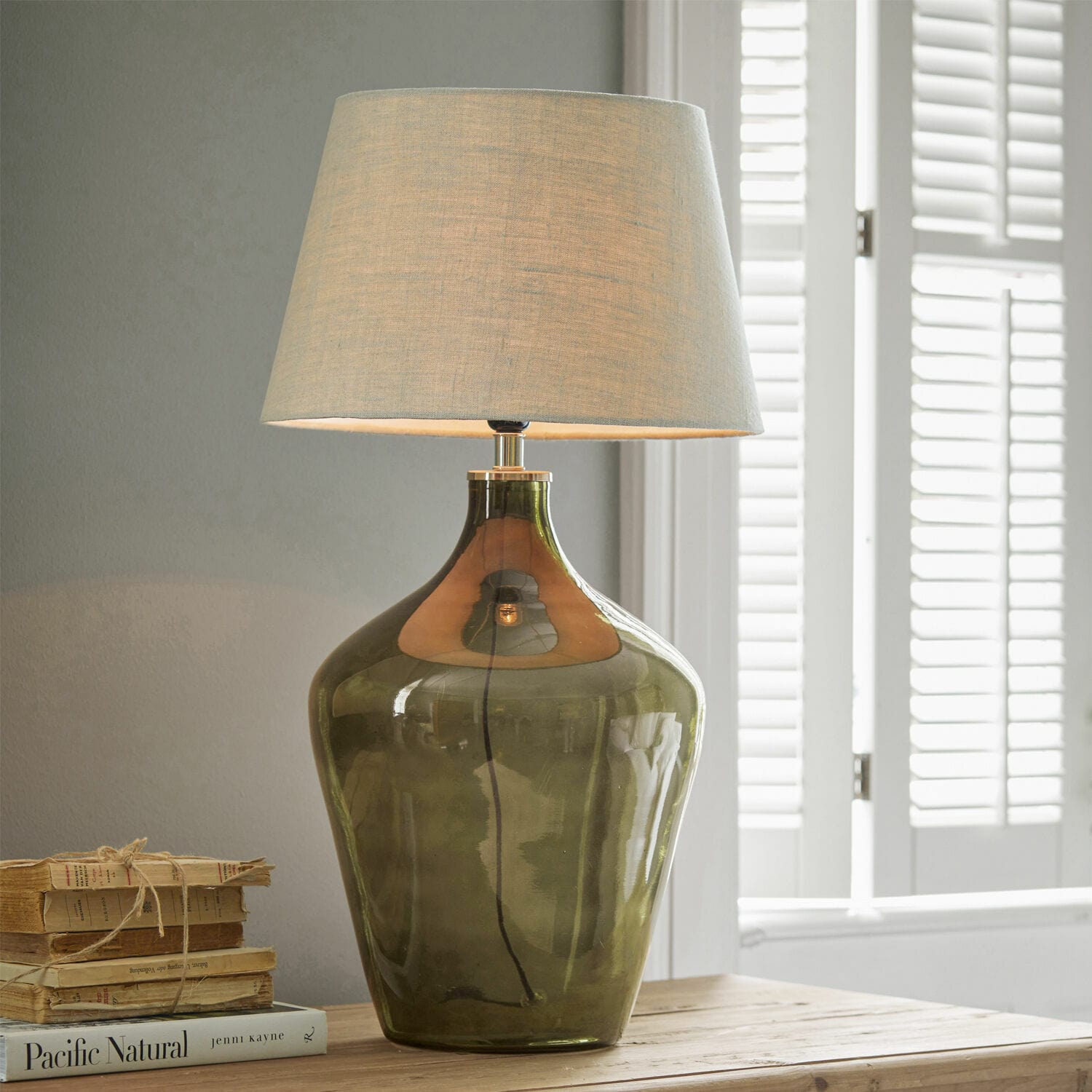 Lampe à poser Morazan Lampe de table en verre vert avec abat-jour beige posée sur une table en bois avec des livres