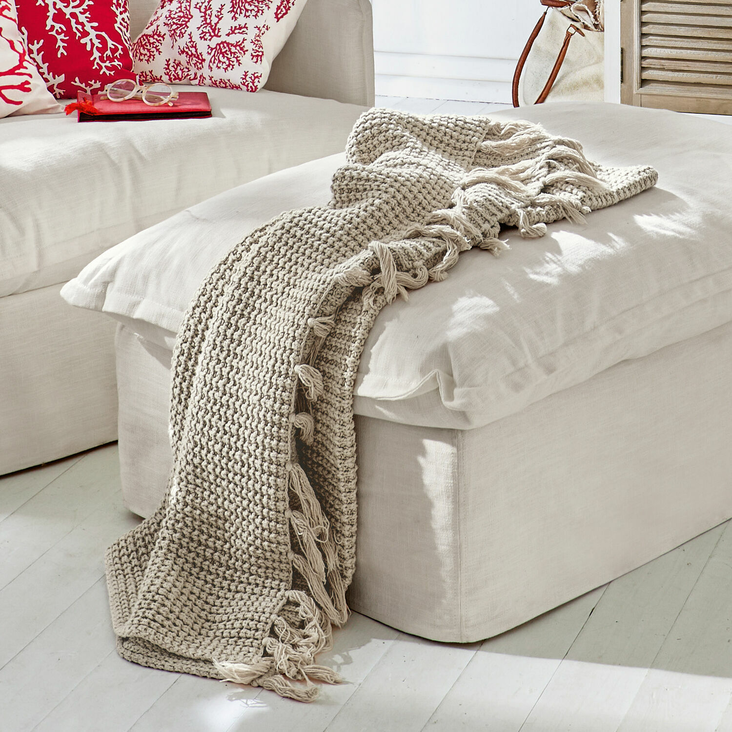 Plaid Kendall Beige gebreide deken met franjes op een lichte poef in een moderne woonkamer