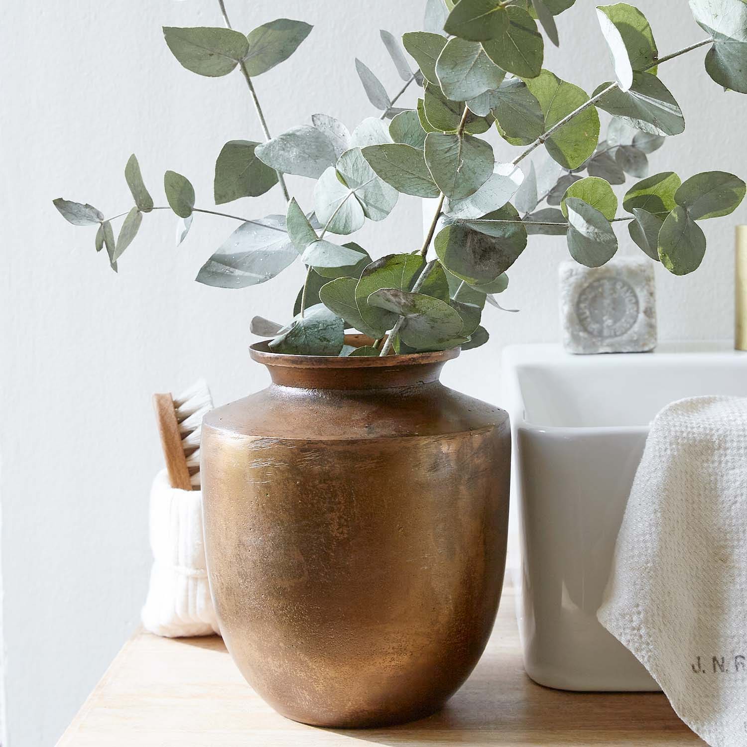 Koperen vaas met groene eucalyptusbladeren op houten blad in lichte kamer