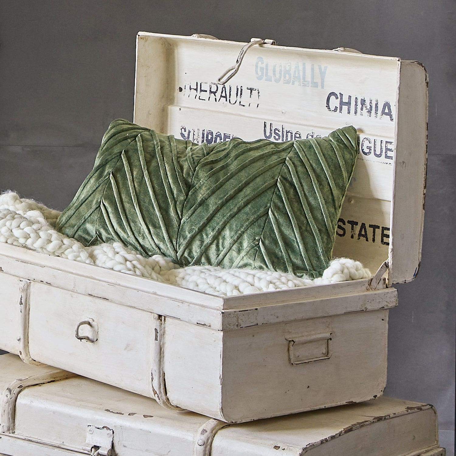 Groen fluwelen kussen met decoratieve stiksels in een witte, verouderde houten kist