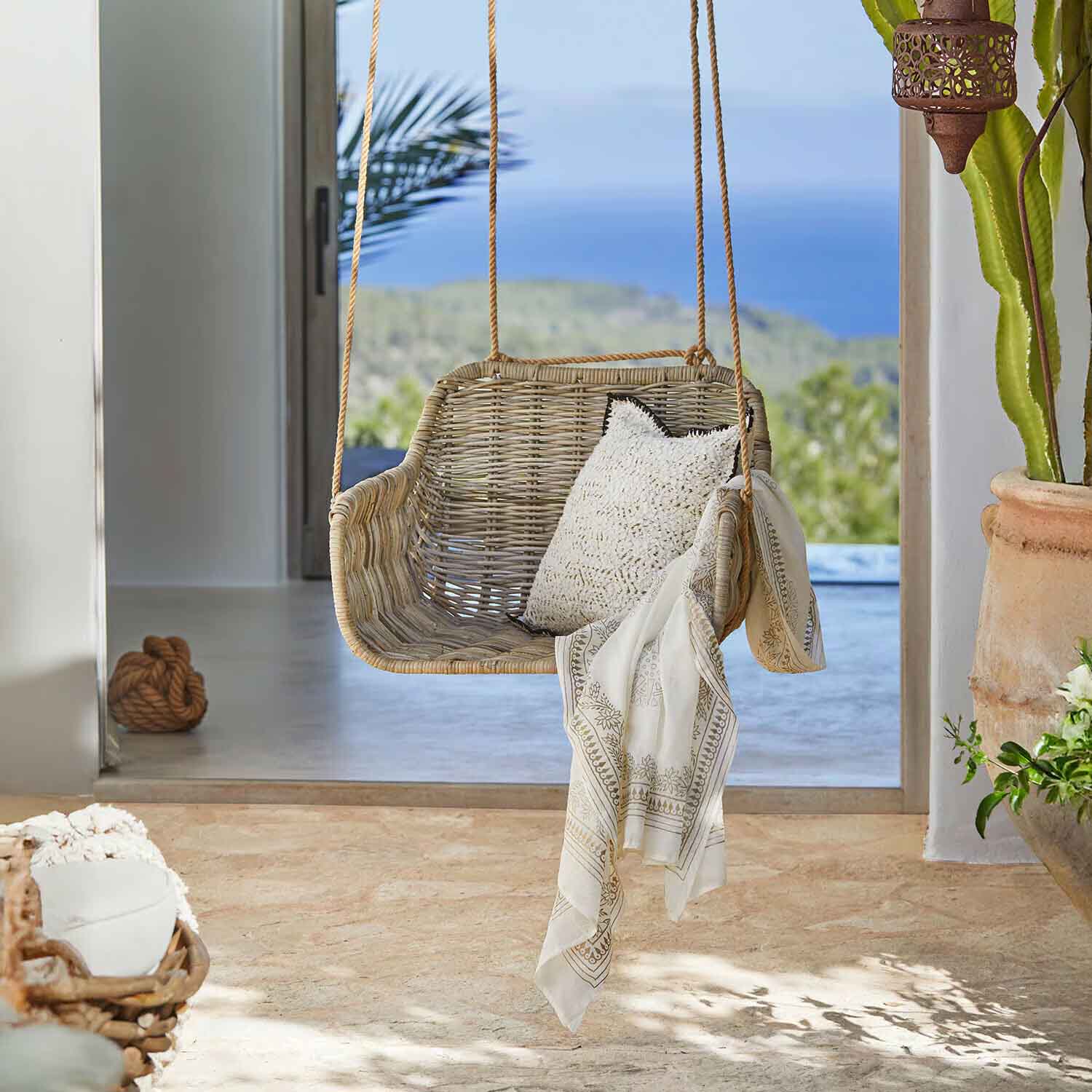 Rotan schommel in natuurlijke kleur met wit kussen en decoratieve sjaal in lichte ruimte
