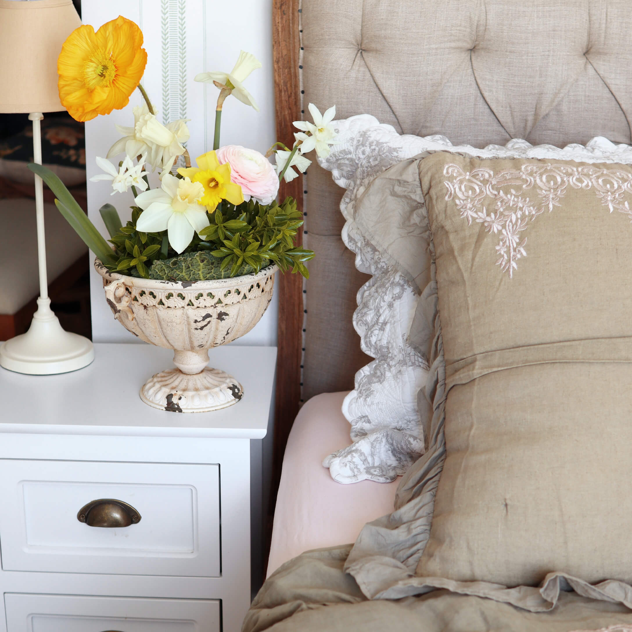 Decoratieve witte keramische vaas met kleurrijke bloemen op een wit nachtkastje naast het bed