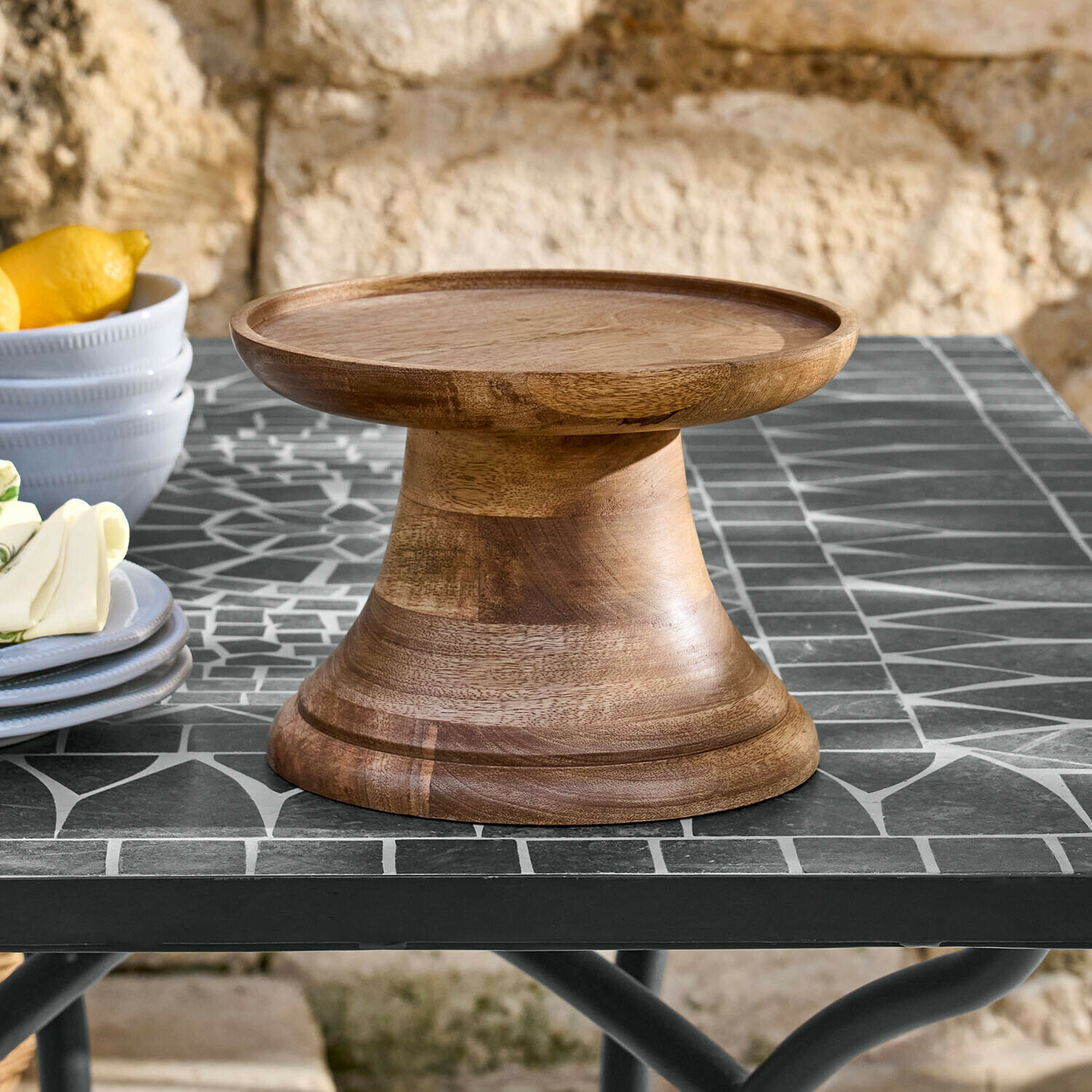 Plateau en bois naturel sur pied posé sur une table en mosaïque, idéal pour présenter gâteaux et desserts