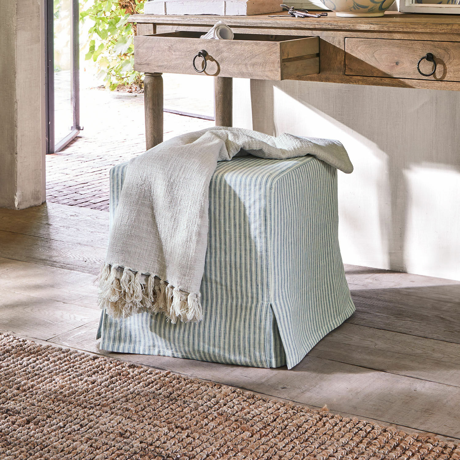 Pouf Ulysette Pouf carré en coton rayé bleu et blanc avec plaid crème sur sol en bois clair