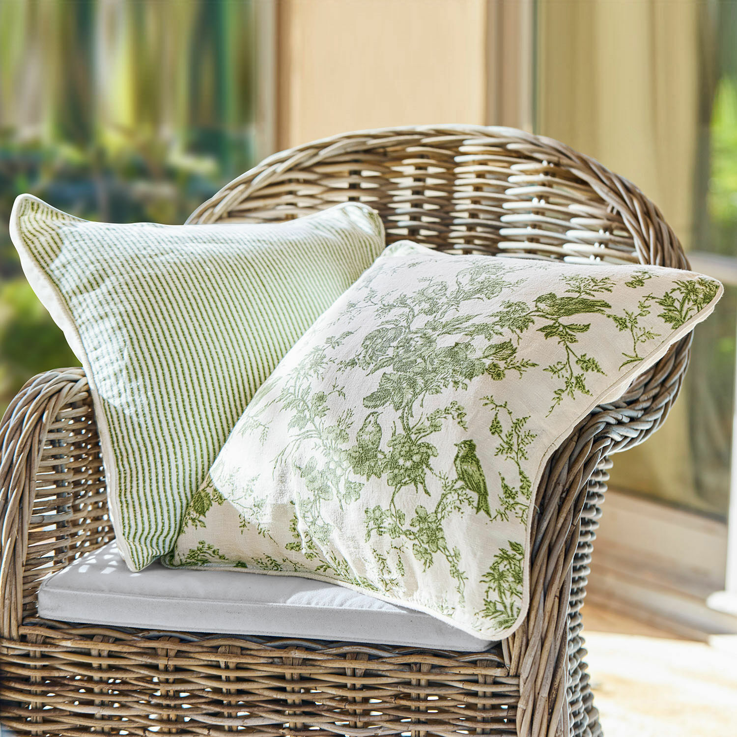 Lot de 2 housses de coussins Mercier Deux coussins décoratifs verts en coton sur un fauteuil en osier dans un intérieur lumineux