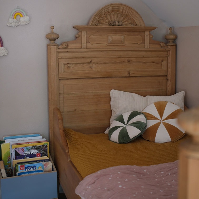Lit de bois massif avec tête de lit sculptée, coussins décoratifs et livres dans une chambre d'enfant