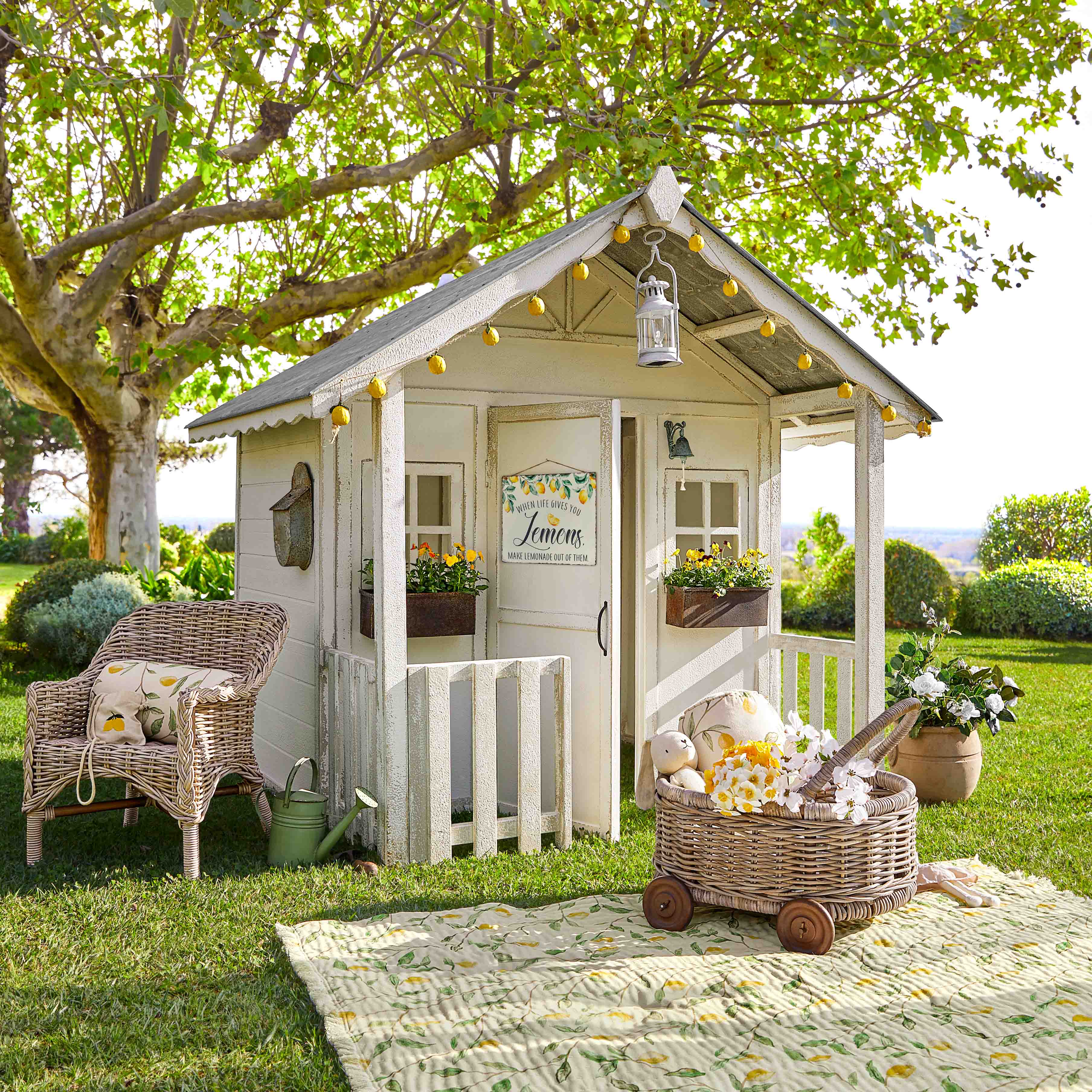 Maisonnette de jardin en bois blanc avec guirlande lumineuse et fleurs sur pelouse verte