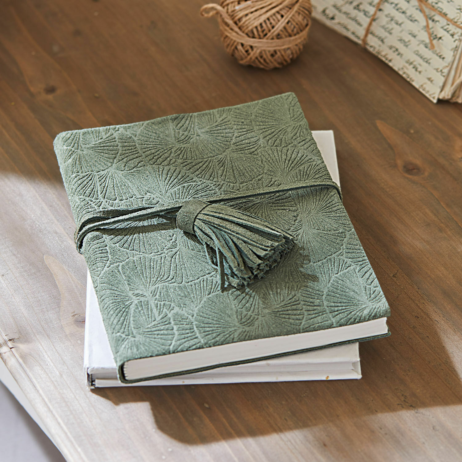 Carnet vert en daim avec motif embossé et pompon sur une table en bois, accessoires d'écriture
