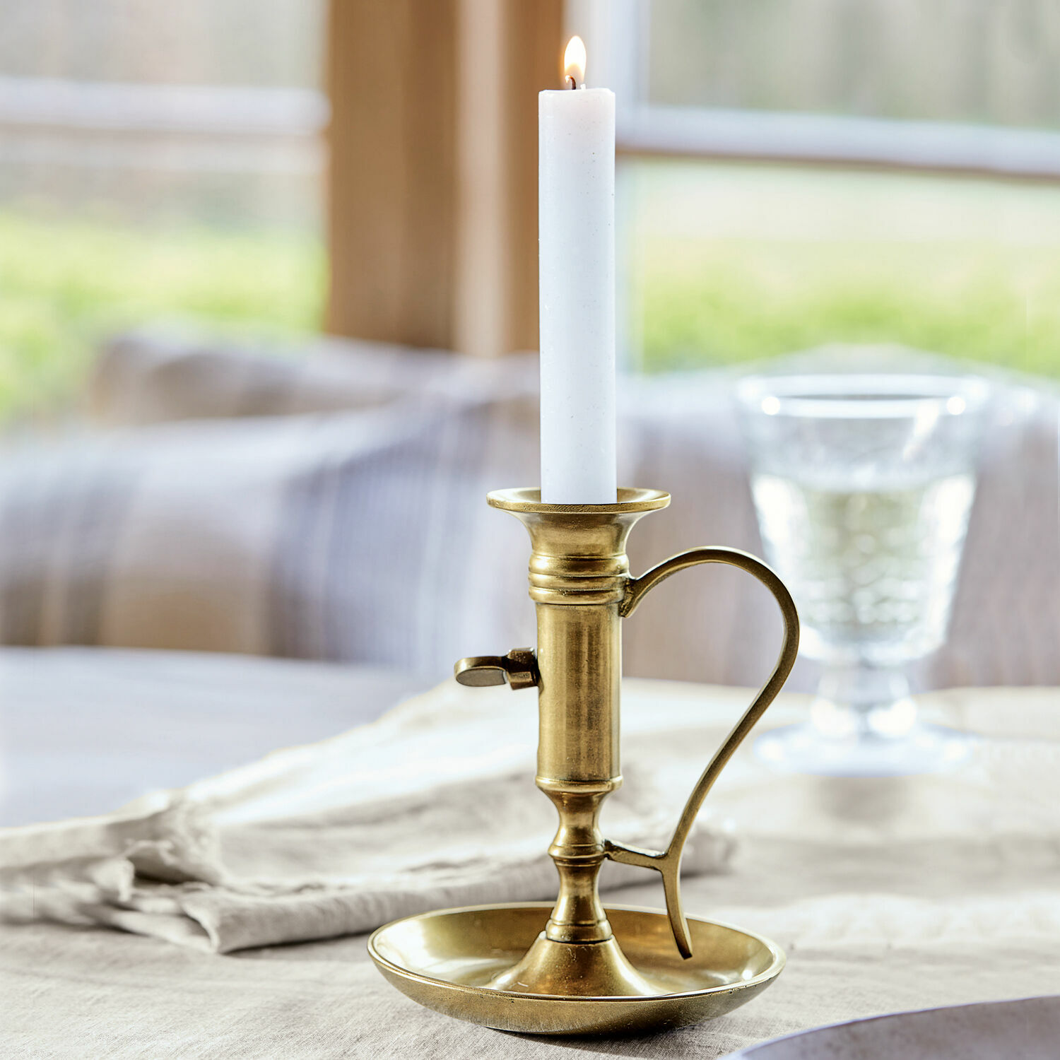 Messing kandelaar met handvat en witte kaars op linnen tafelkleed, tafeldecoratie