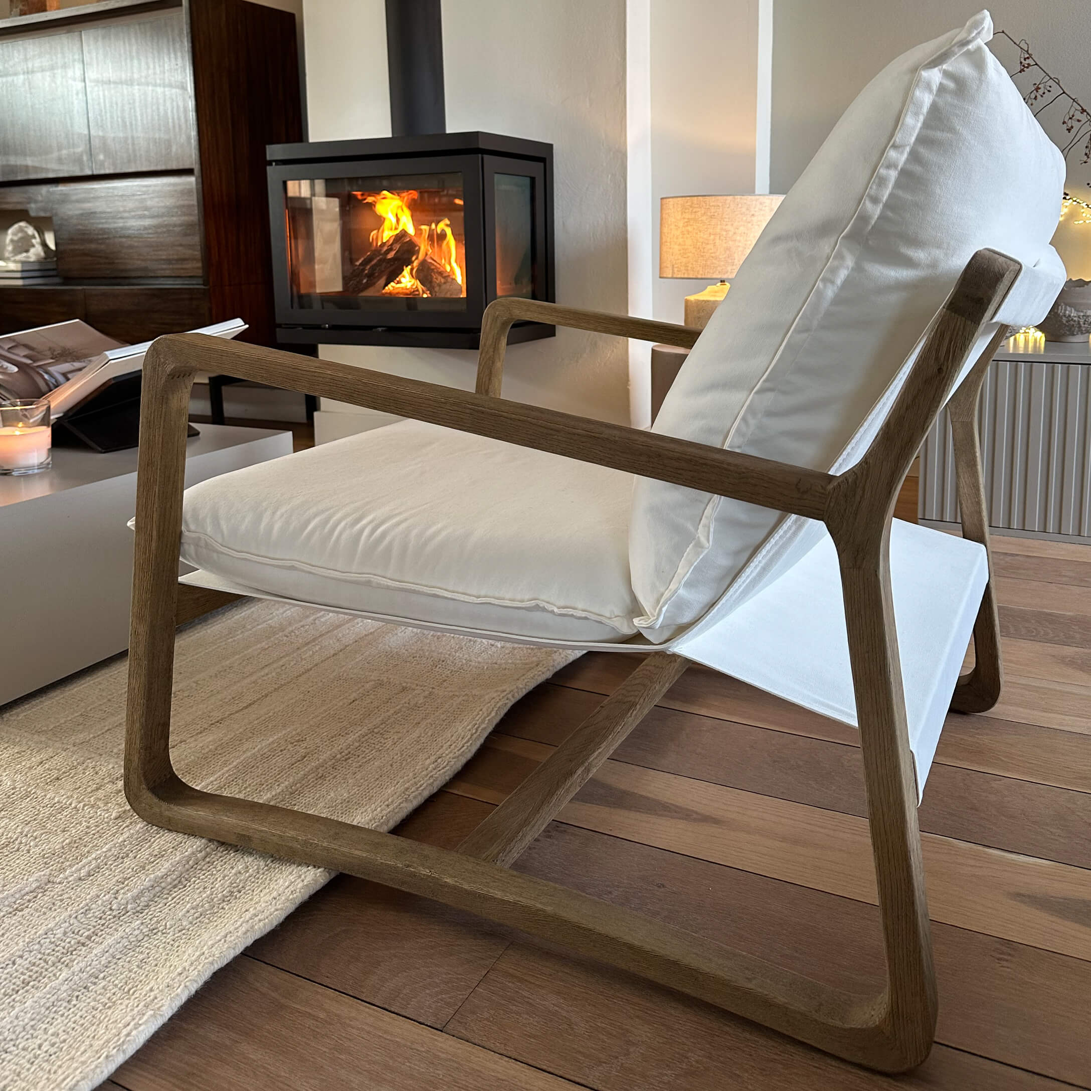 Fauteuil moderne en bois avec coussins blancs dans un salon chaleureux avec cheminée allumée