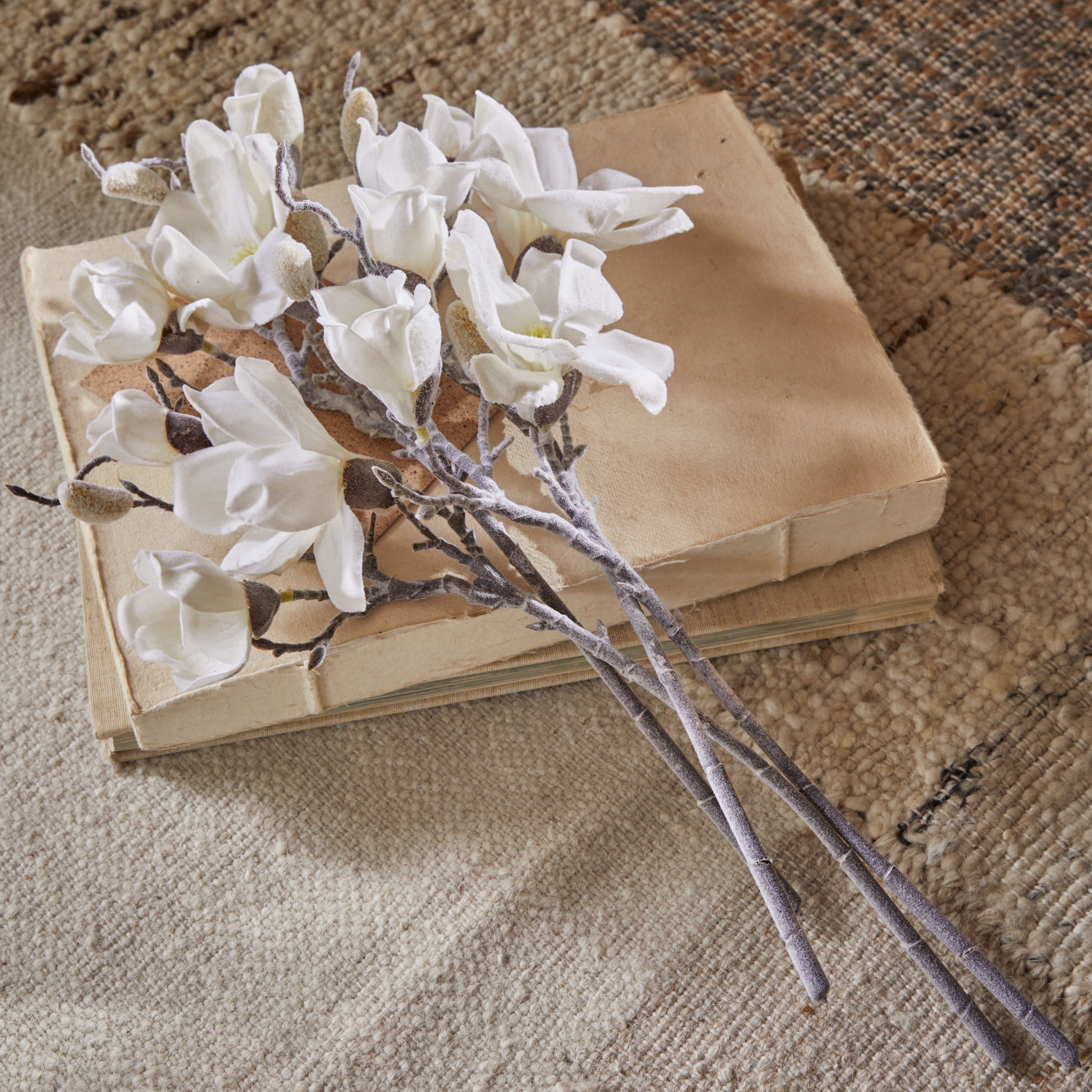 Boeket witte magnoliabloemen van stof op oude beige boeken op een vloerkleed