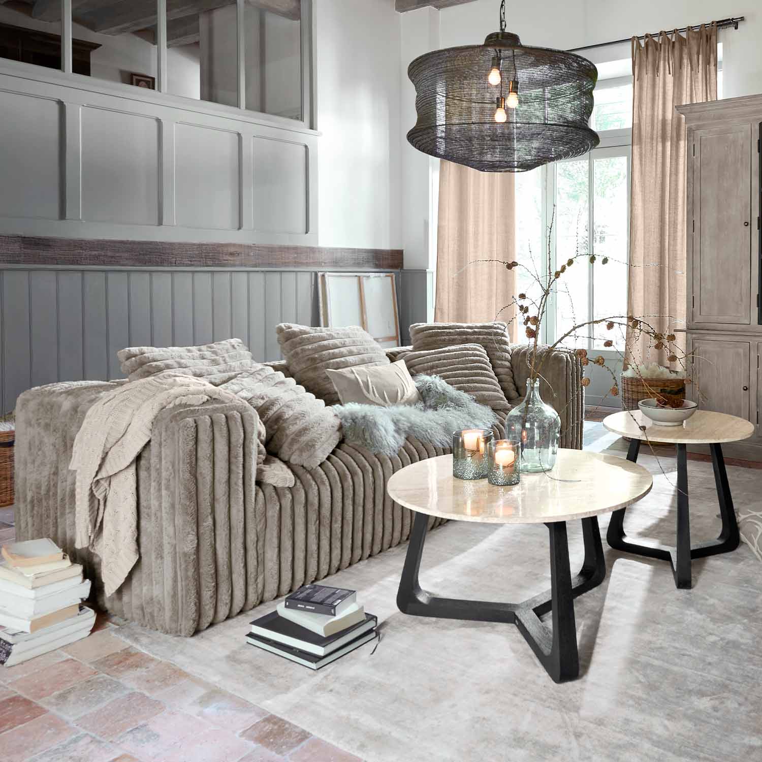 Canapé beige en tissu doux dans un salon moderne avec deux tables basses rondes en bois et métal