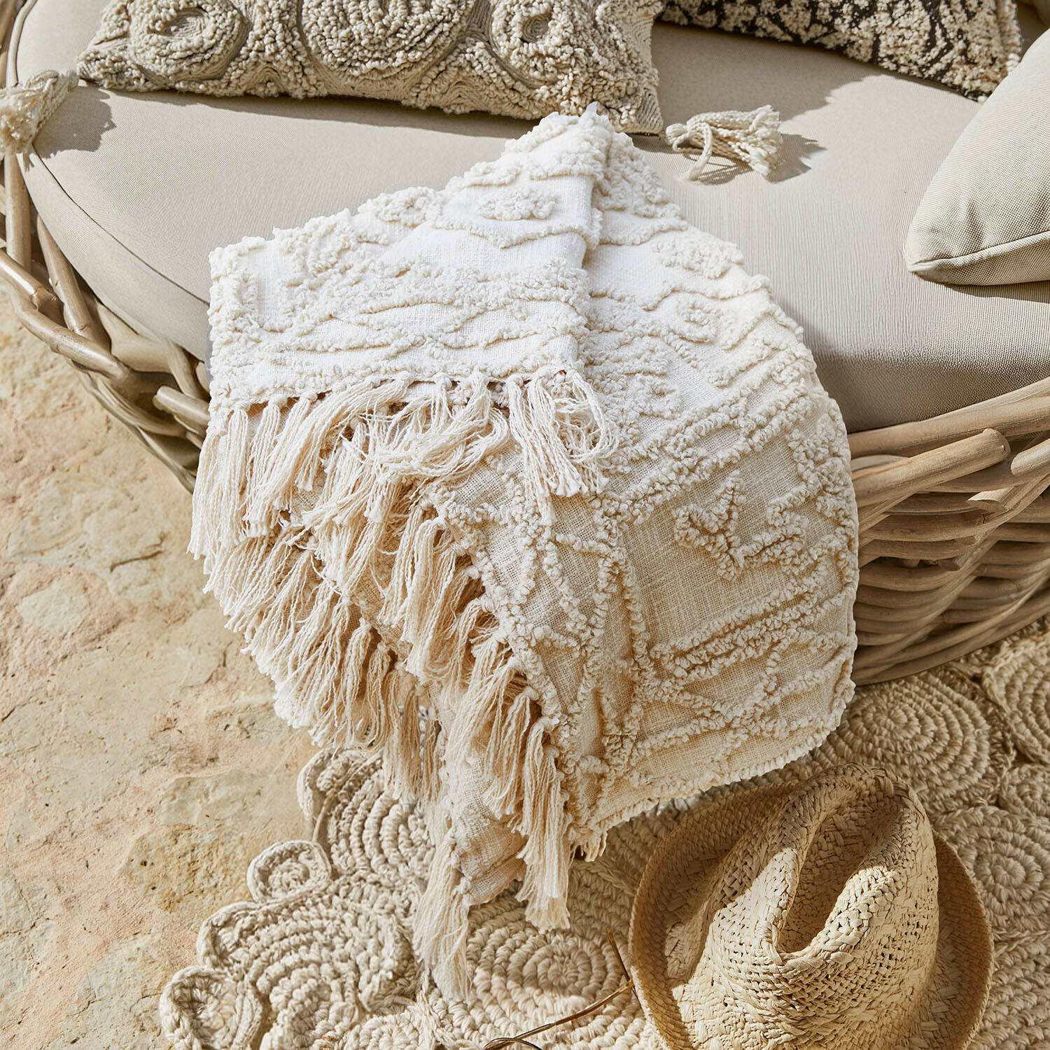 Plaid Norlinn Beige decoratief deken met franjes op rotan stoel en strohoed op de vloer