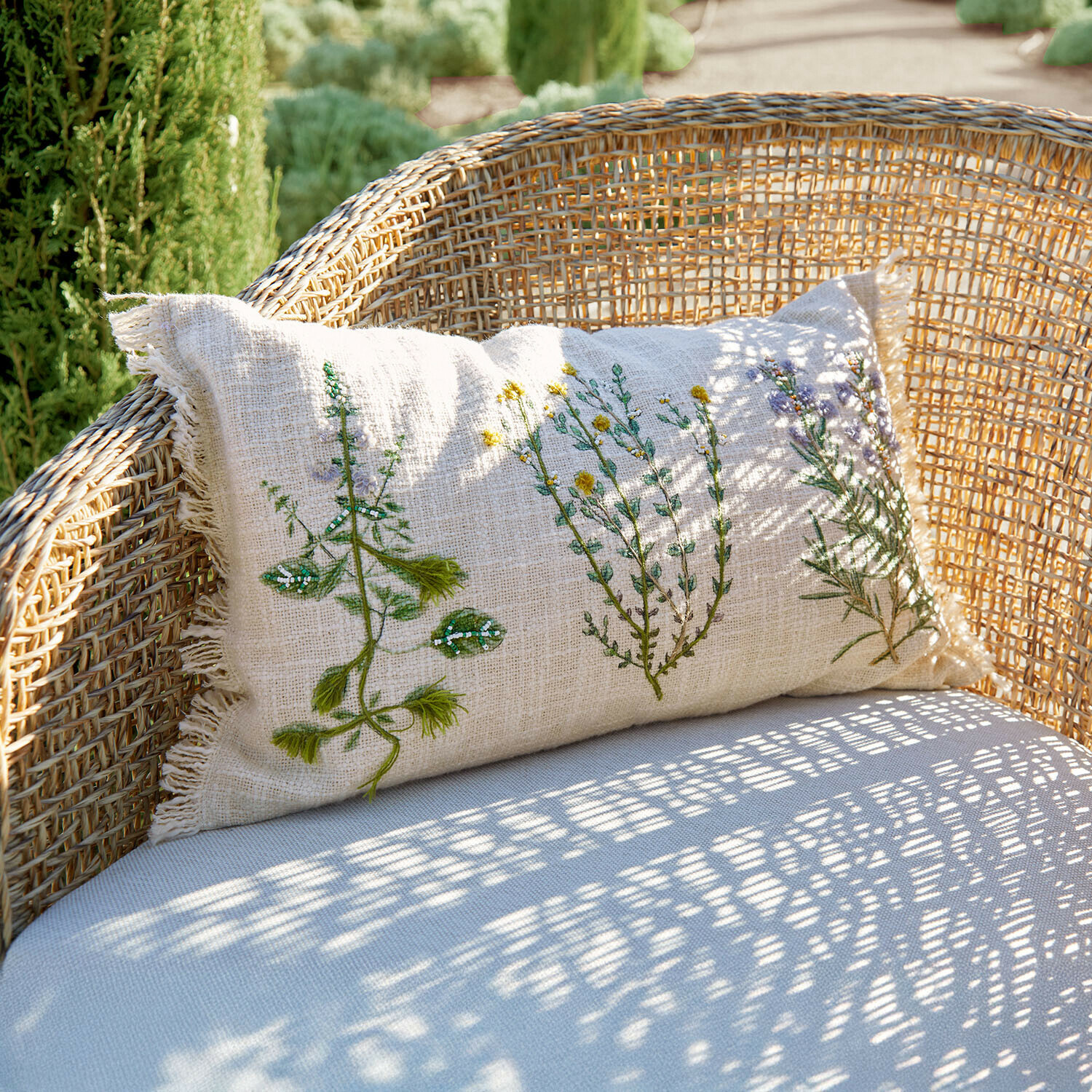 Beige linnen kussen met plantenborduursel op rotan stoel, tuinaccessoire