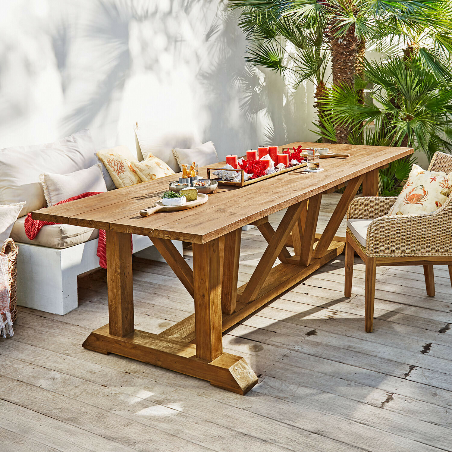 Table Melvoro Grande table à manger en bois de teck naturel sur terrasse avec bougies rouges et apéritifs décoratifs
