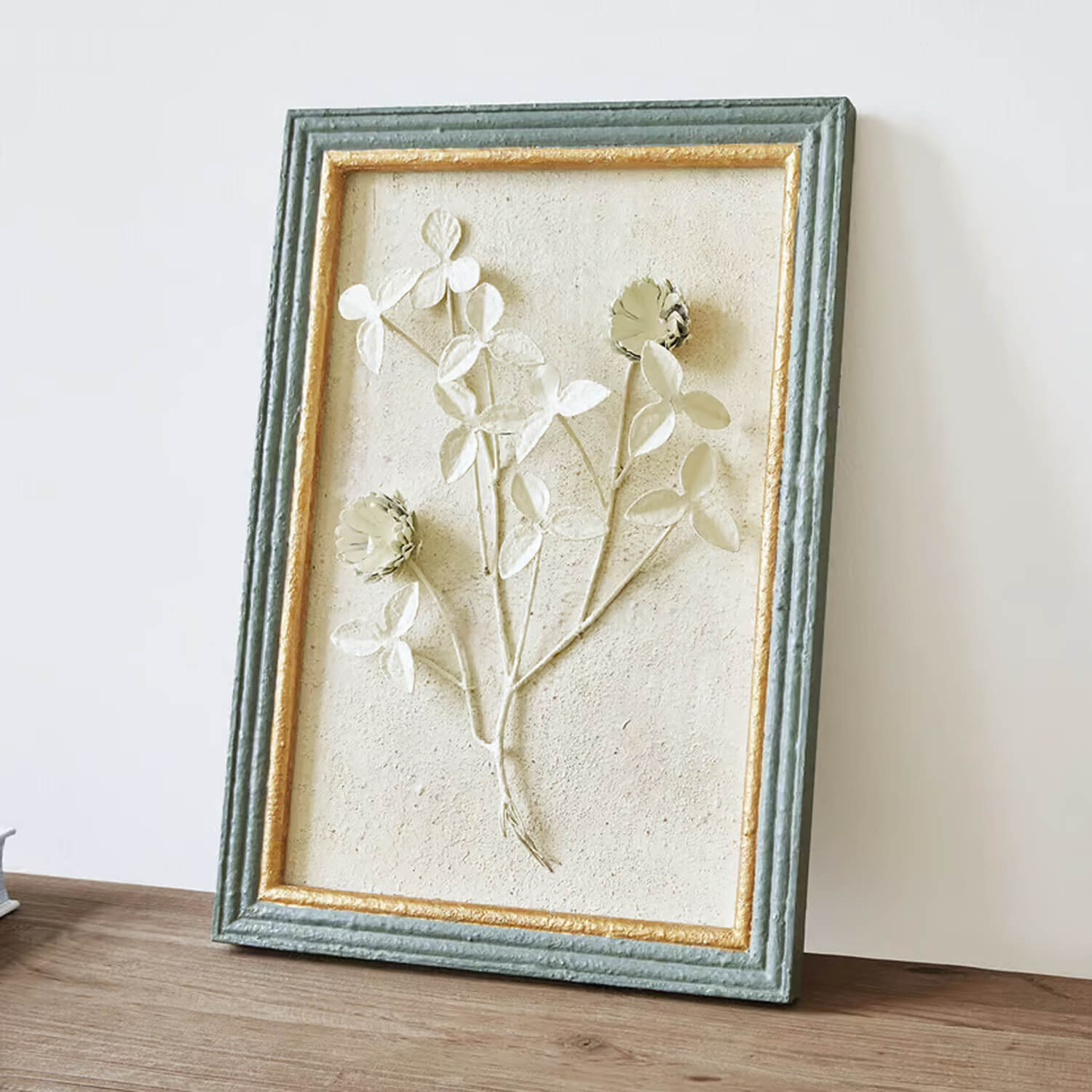 Relief floral décoratif encadré avec texture verte et dorée sur fond beige clair