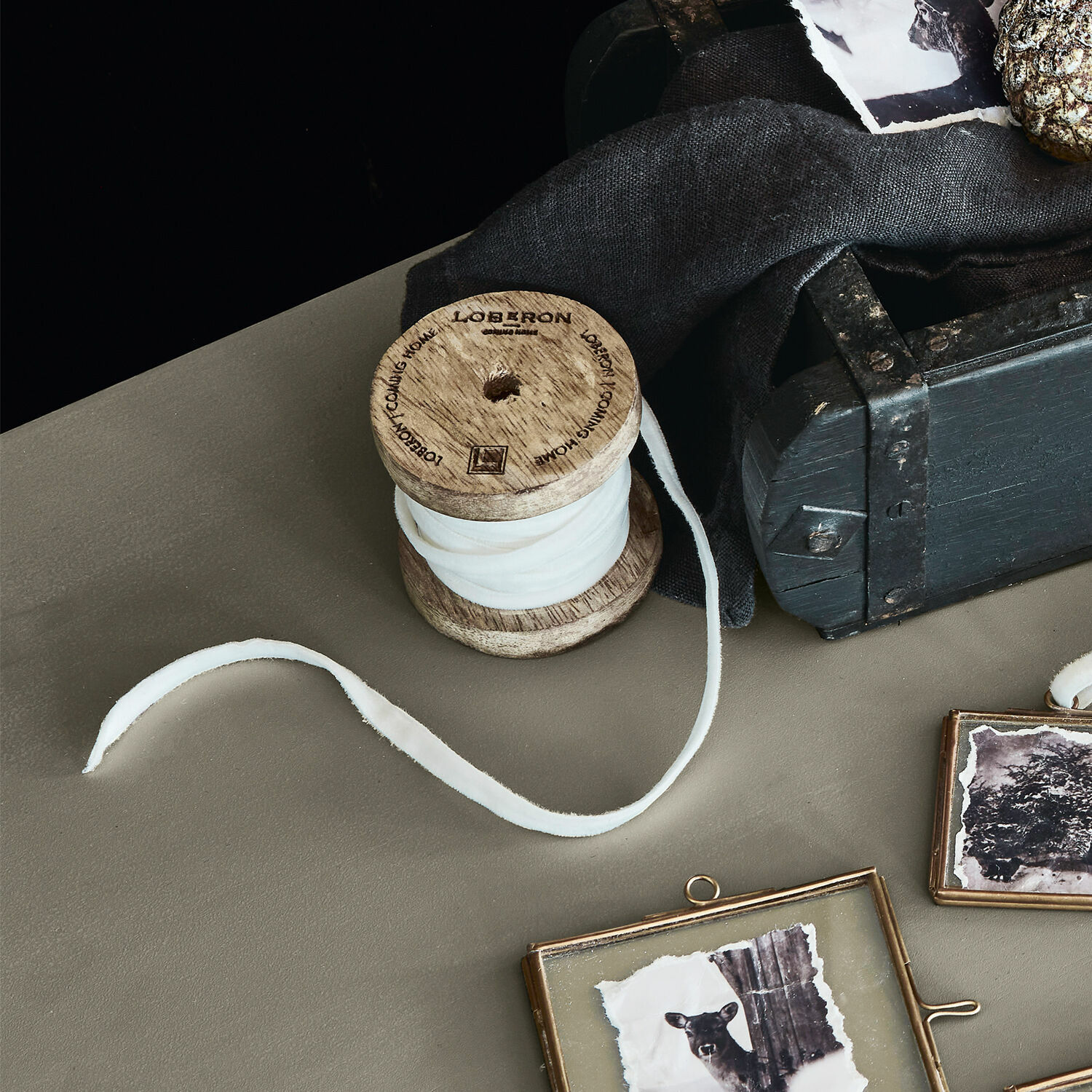 Ruban de velours Olessa Bobine en bois avec tissu blanc sur table près d'une boîte noire et cadres photo décoratifs
