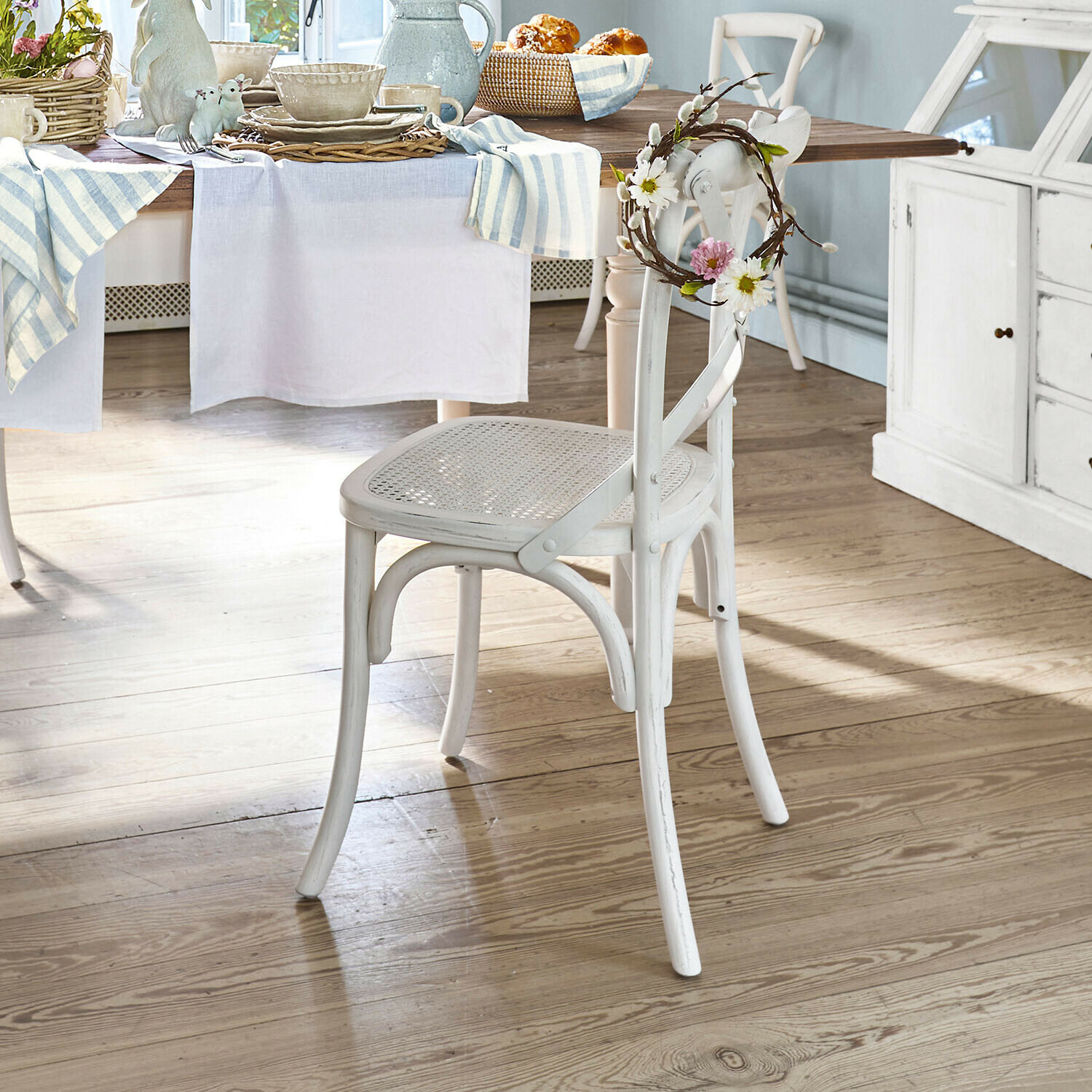 Chaise en bois blanc avec assise en osier et couronne florale décorative dans une salle à manger lumineuse