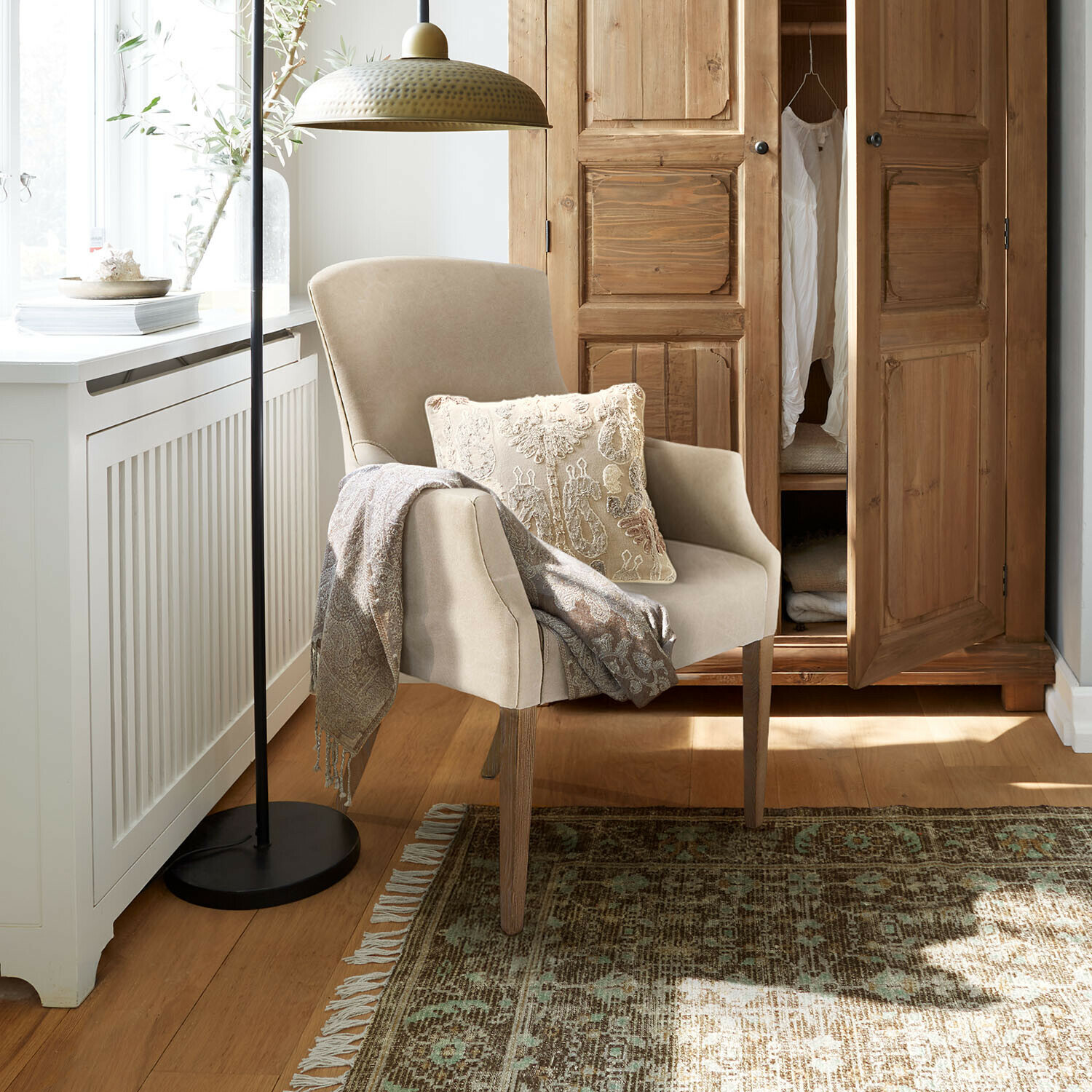 Beige fauteuil met houten poten, decoratief kussen en deken in een gezellige woonkamer met houten kast