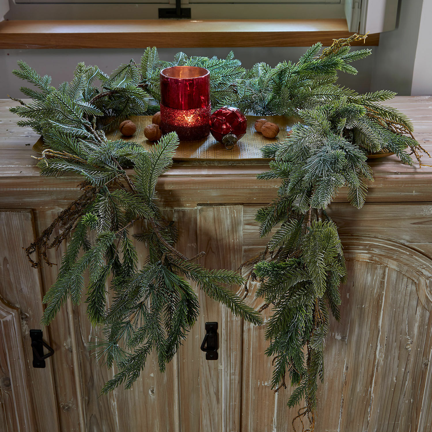 Guirlande Dolomera Decoratieve krans van groene dennentakken met rode kandelaar en noten op houten kast