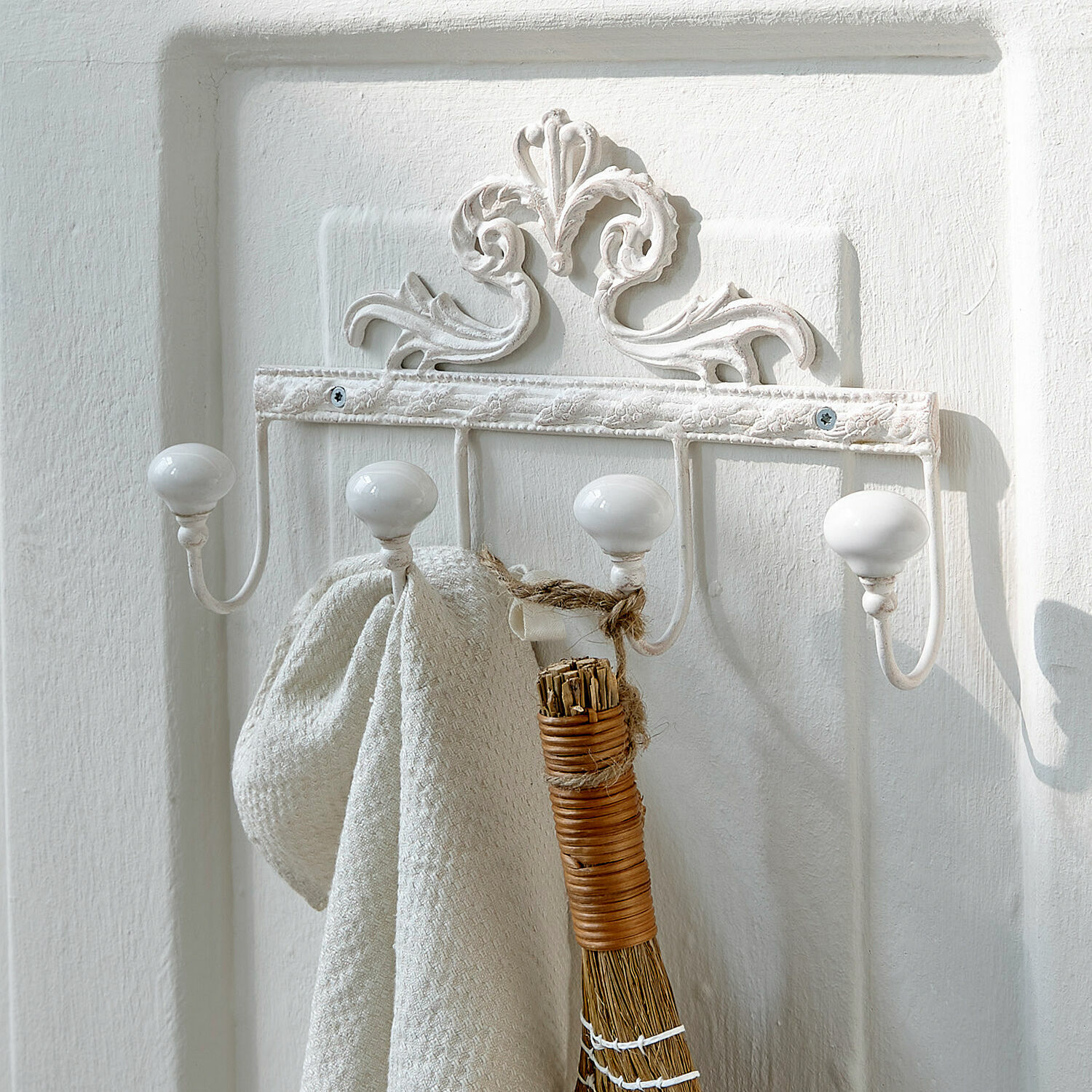 Witte metalen wandkapstok met keramische knoppen en decoratief patroon, voor de hal