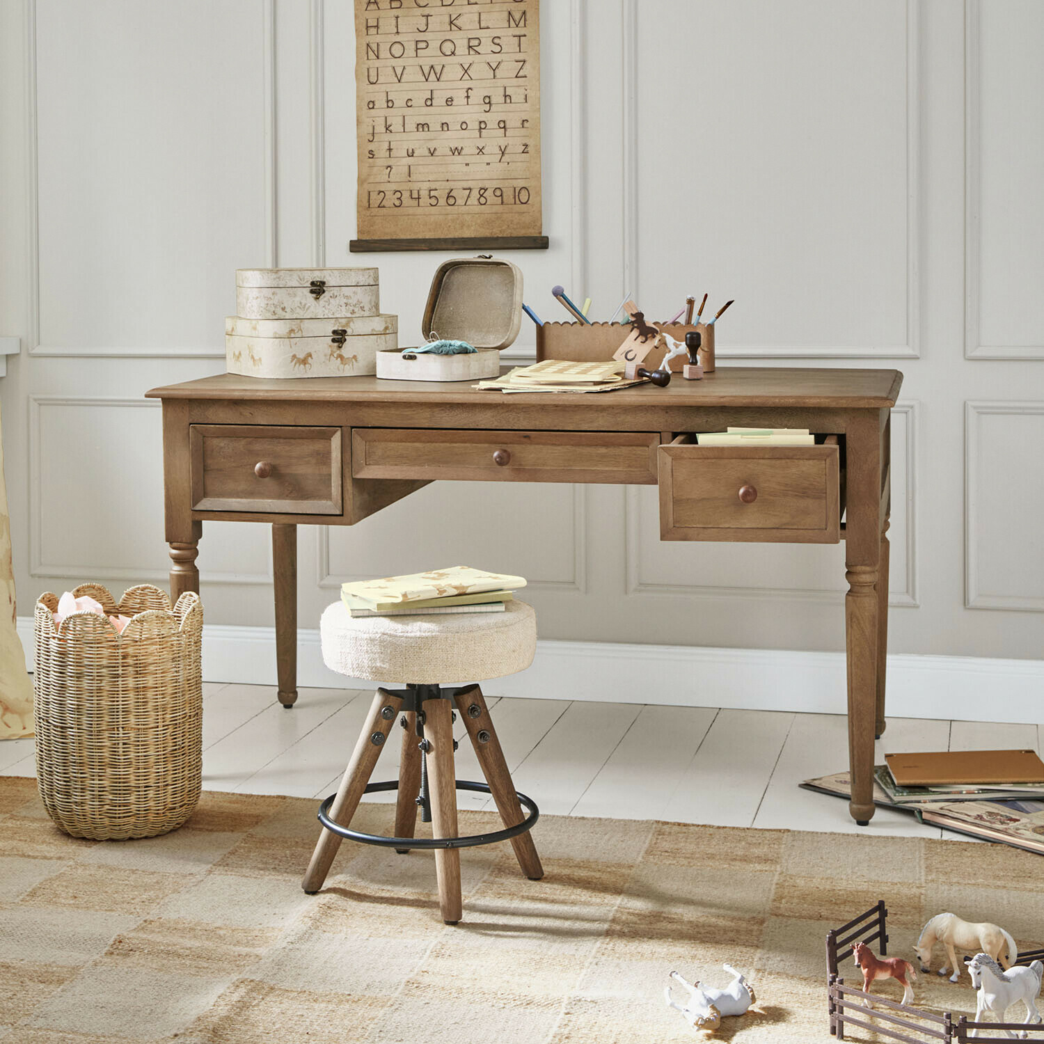 Kinderbureau Norleigh Houten bureau met drie lades en beige kruk in lichte kamer met educatieve decoraties